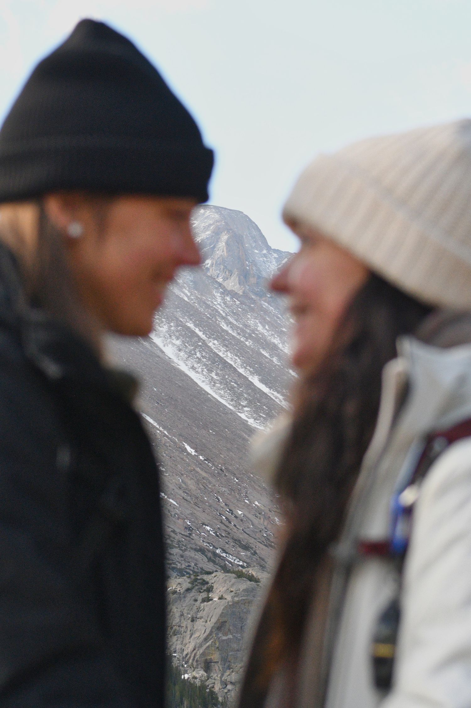 Couple, out of focus, with Longs Peak, in focus, between them. Pixcapades | The Rocky Mountain Proposal Photographer