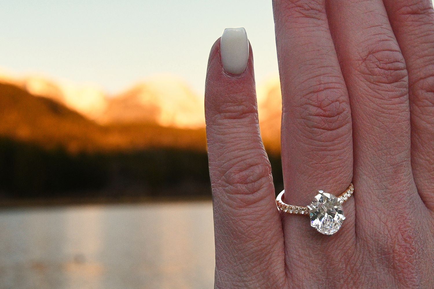 Her engagement ring with alpenglow lit mountains and Sprague Lake in the background. Pixcapades | The Rocky Mountain Proposal Photographer