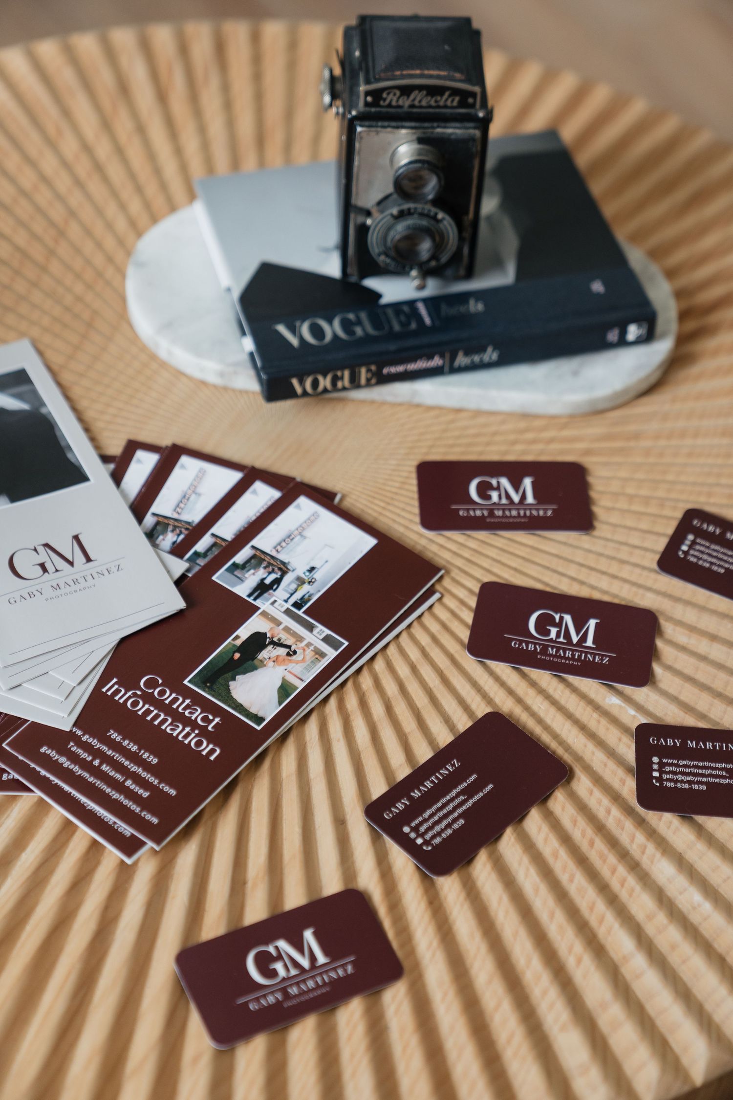GM Gary Martinez branded business cards displayed on a table with Vogue books and a vintage Rolleiflex camera.