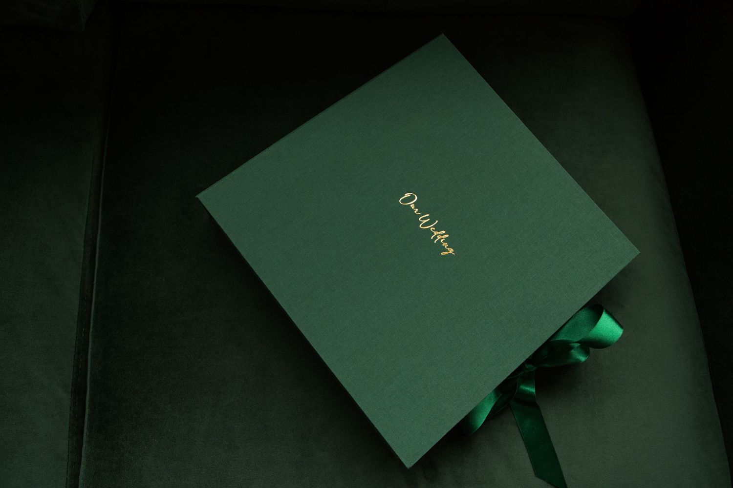 A dark green luxury gift box with gold lettering sits elegantly on a black background with a ribbon peeking out.