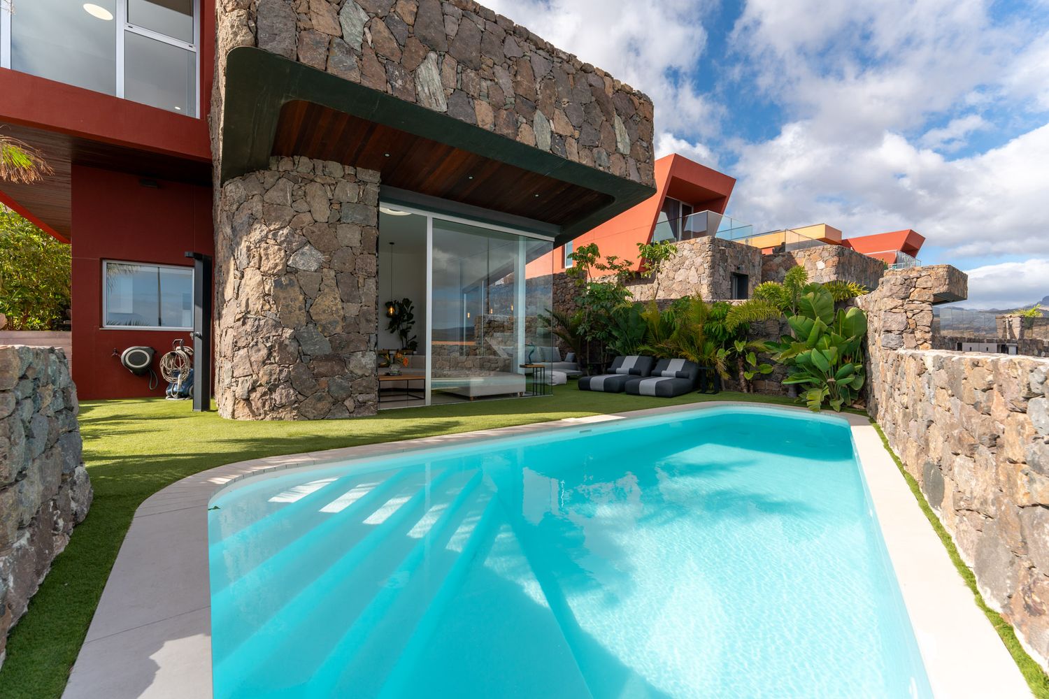 Modern luxury villa with stone walls, glass windows and turquoise swimming pool on a sunny day.