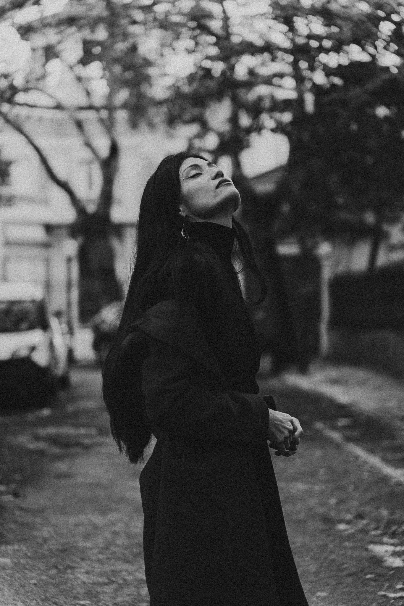 Artistic black and white portrait of person in dark coat with head tilted back.