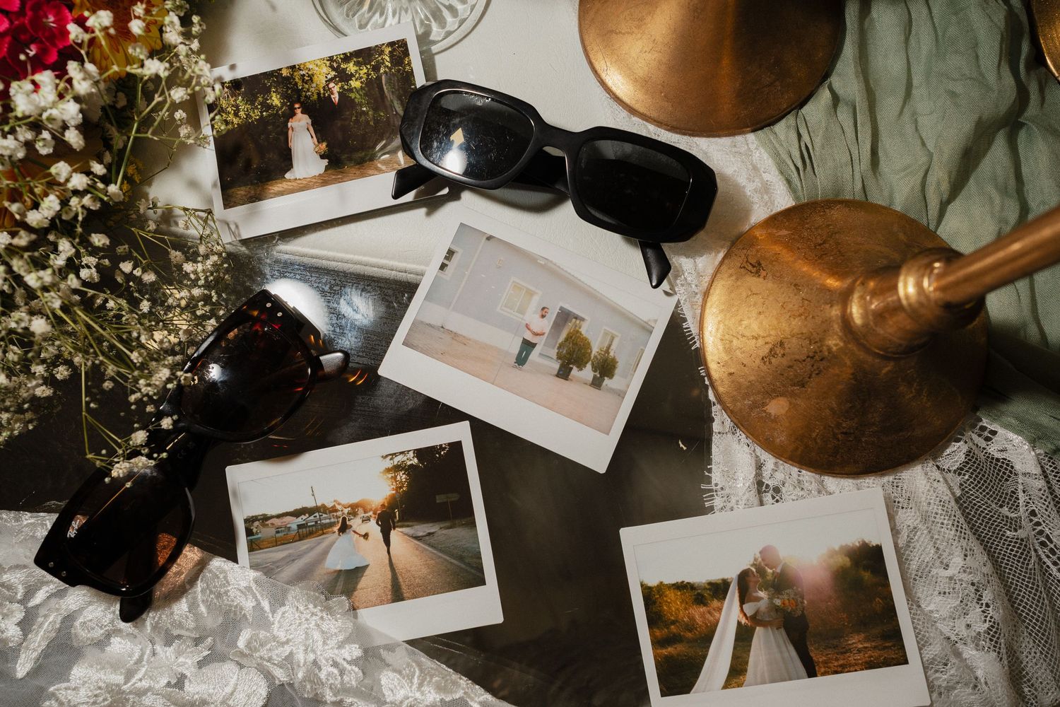 Polaroid photos scattered among dried flowers and vintage decorative items on a rustic wooden surface.