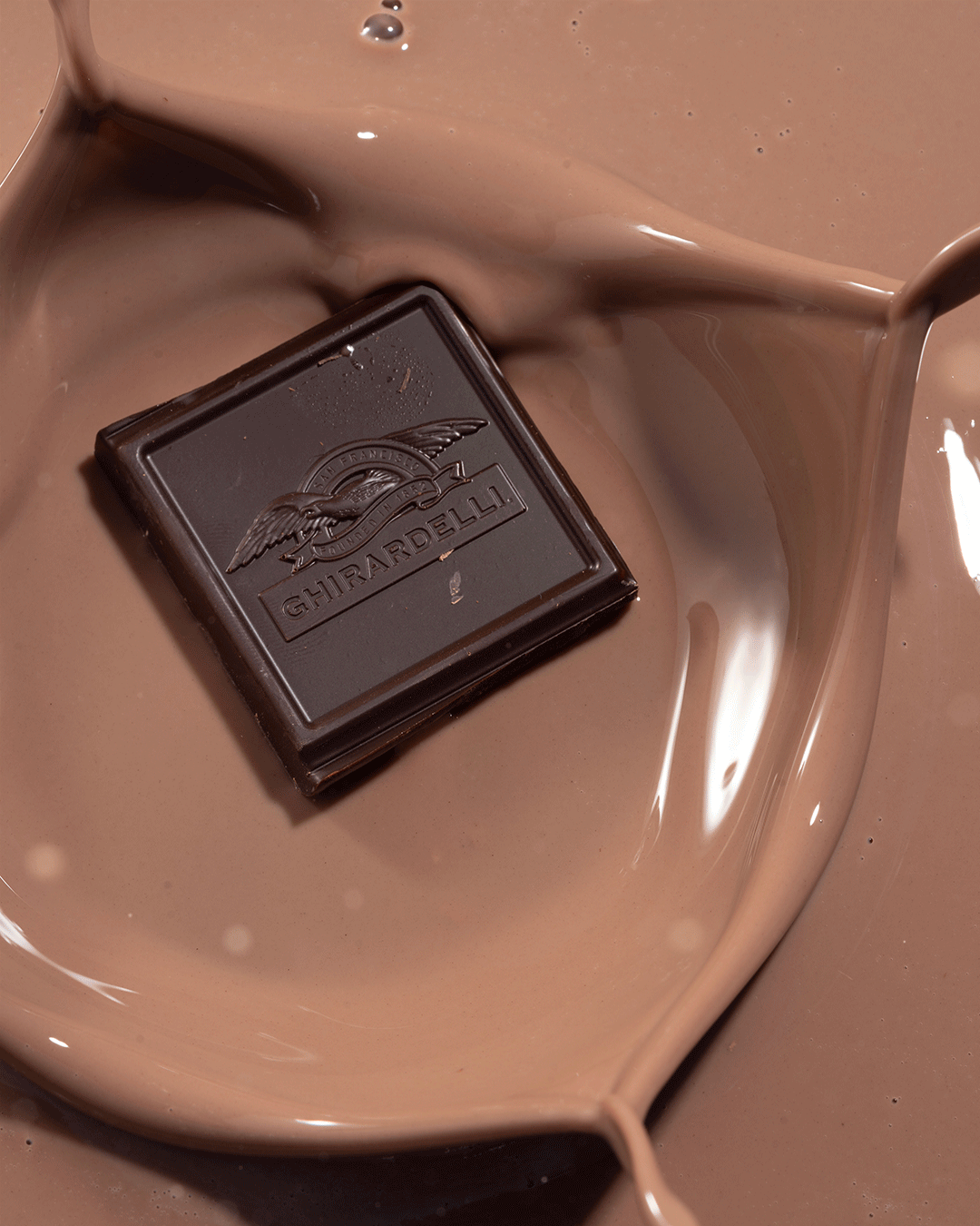 Ghirardelli dark chocolate square resting in a pool of smooth melted milk chocolate.