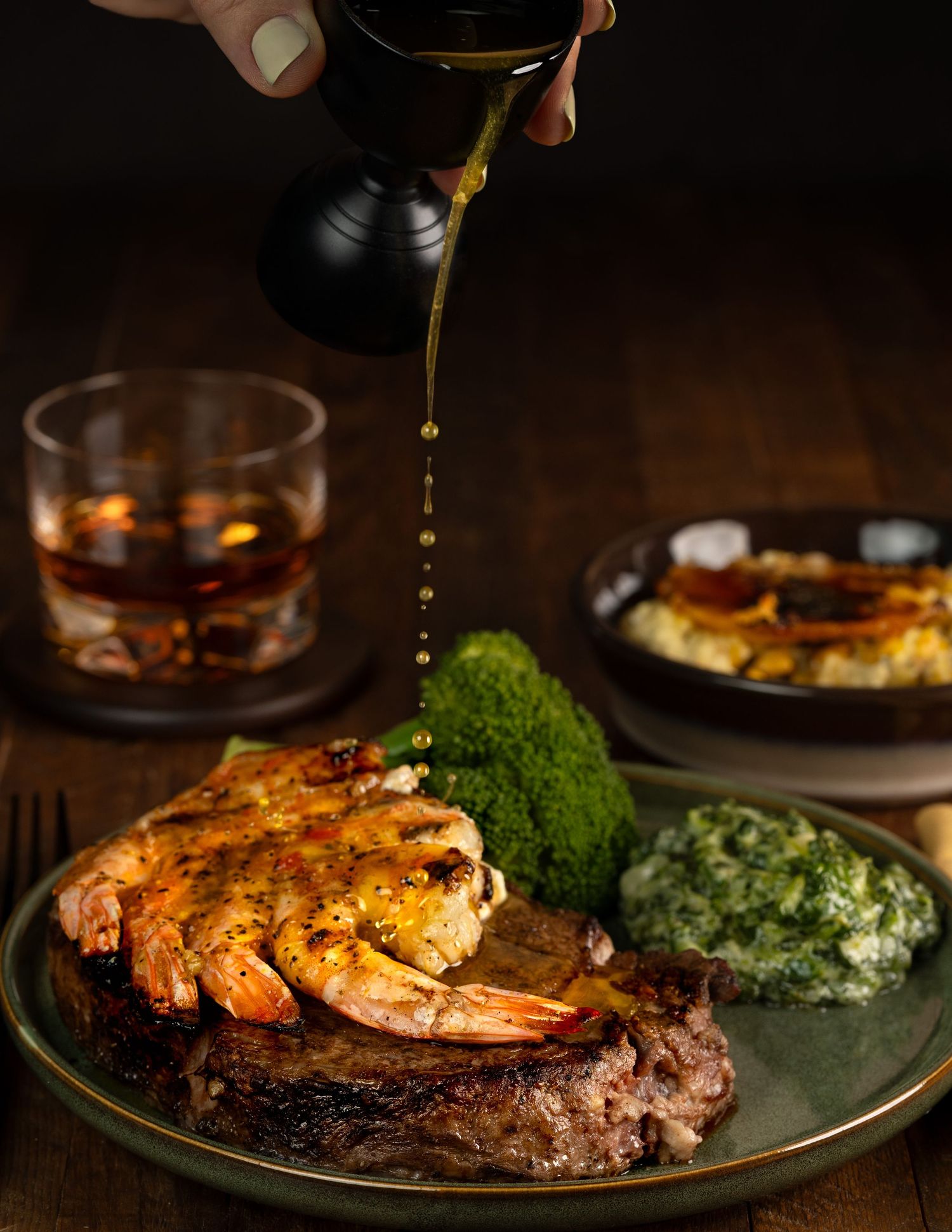 Steak and shrimp surf and turf dinner plate with broccoli, being drizzled with golden butter sauce.