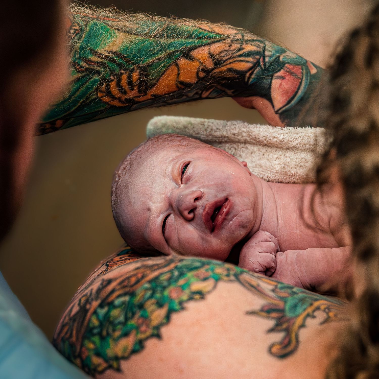 Newborn baby resting against colorful tattoo sleeve after birth.