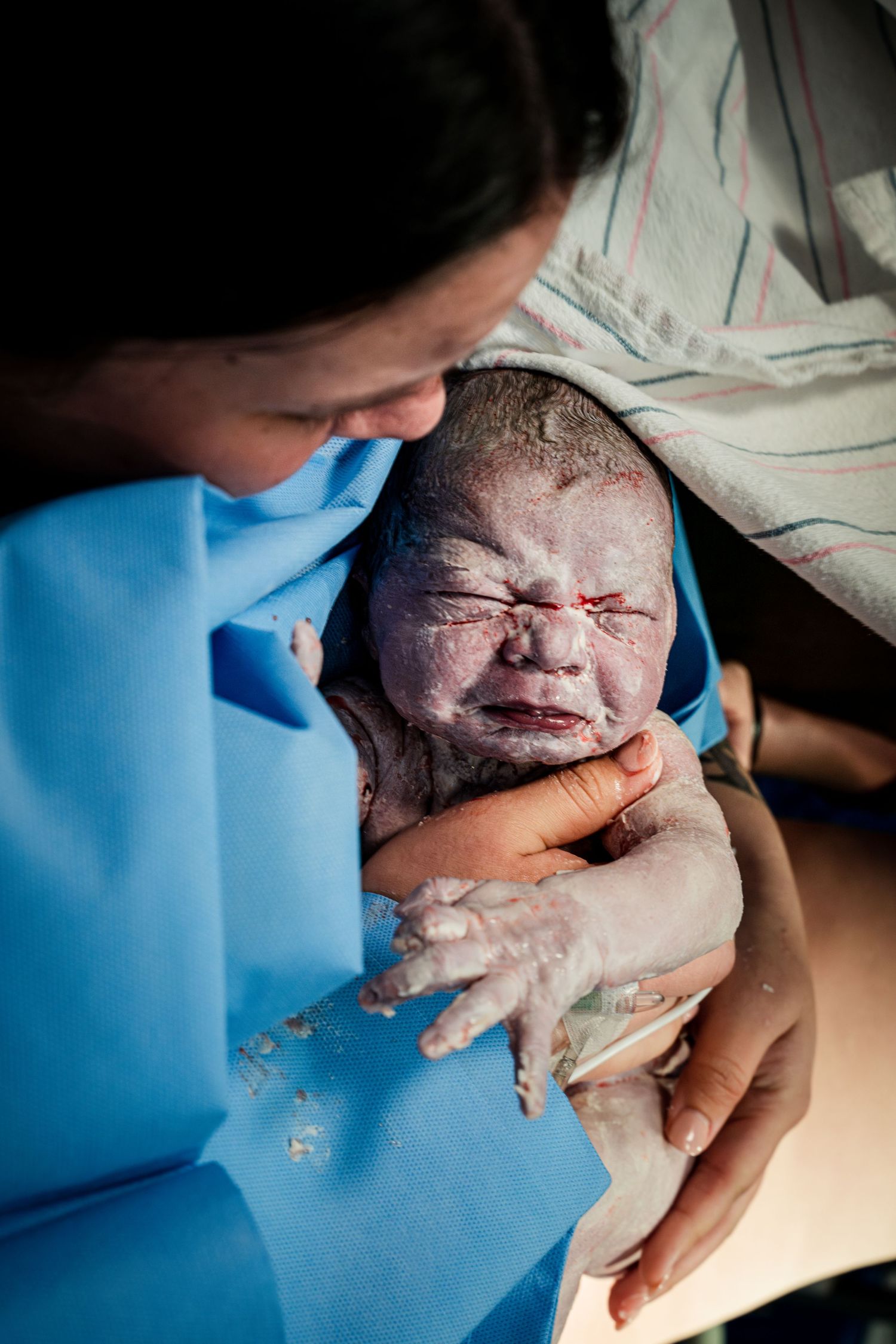 Healthcare worker holds newborn baby displaying first expressions after birth.