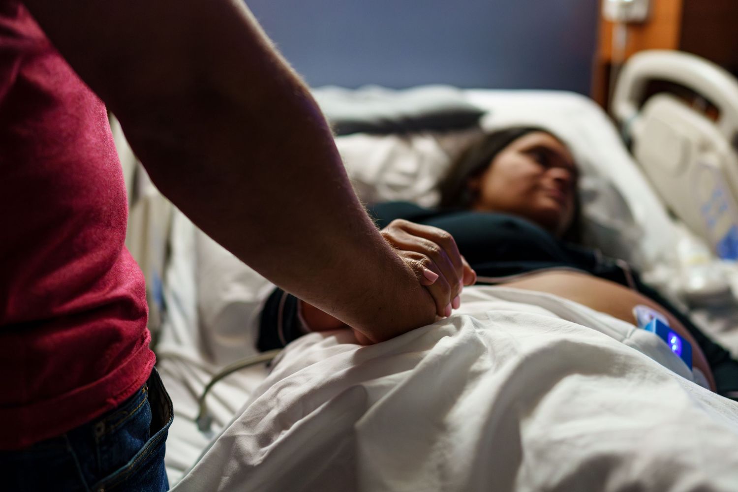 Healthcare worker examines patient in hospital bed while checking medical equipment and monitors.