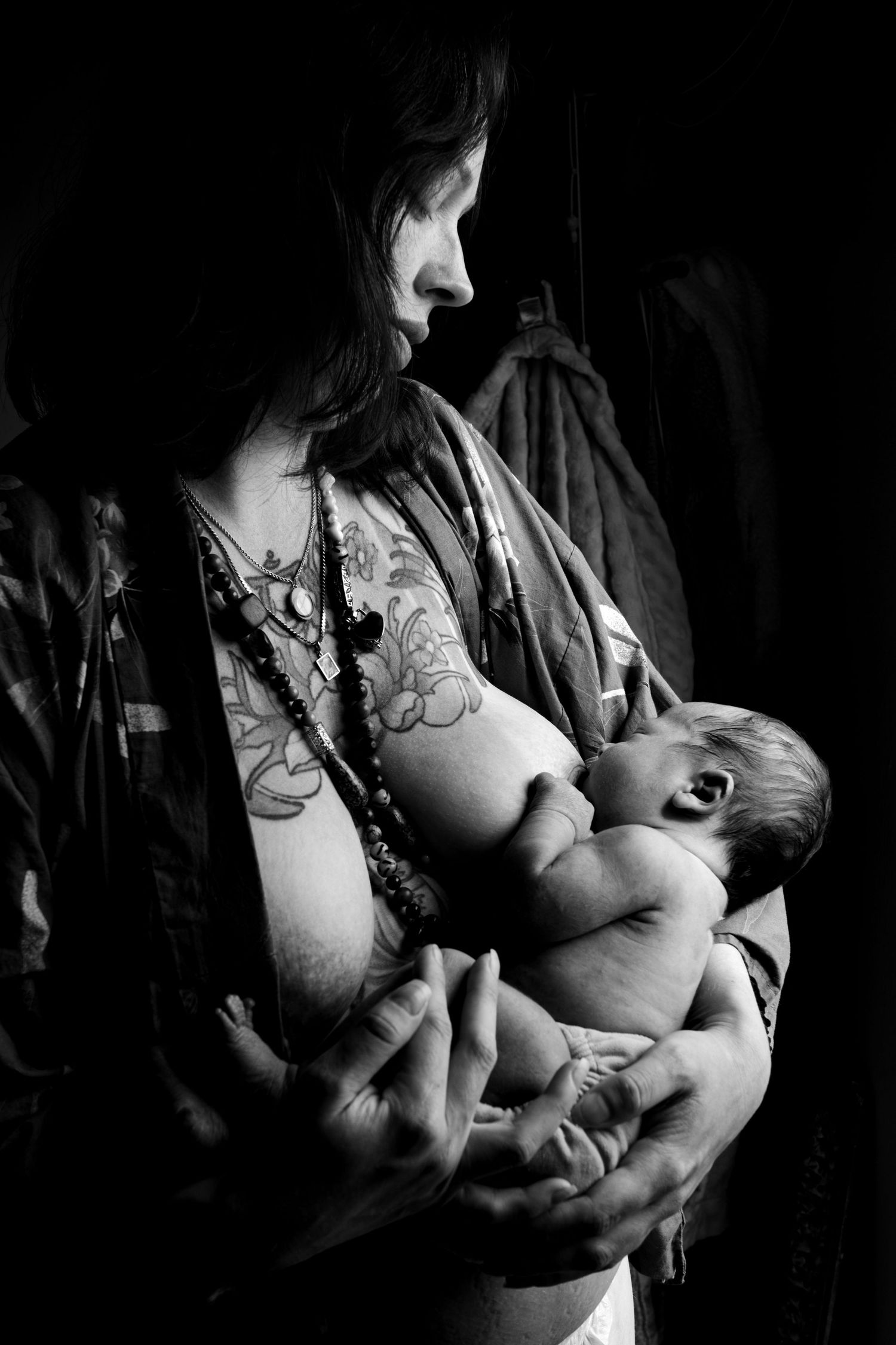 Black and white intimate portrait of mother nursing infant in low light setting during newborn lifestyle photoshoot in New Orleans Louisiana