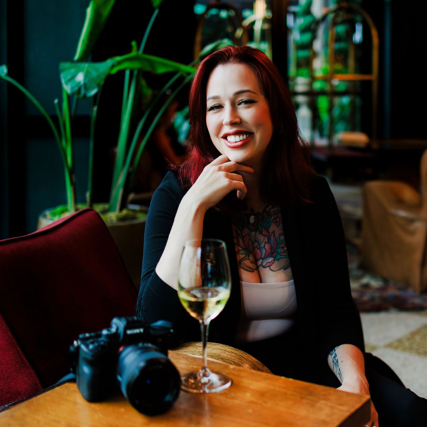 Person relaxing with a glass of wine at a cozy restaurant with green plants in background.