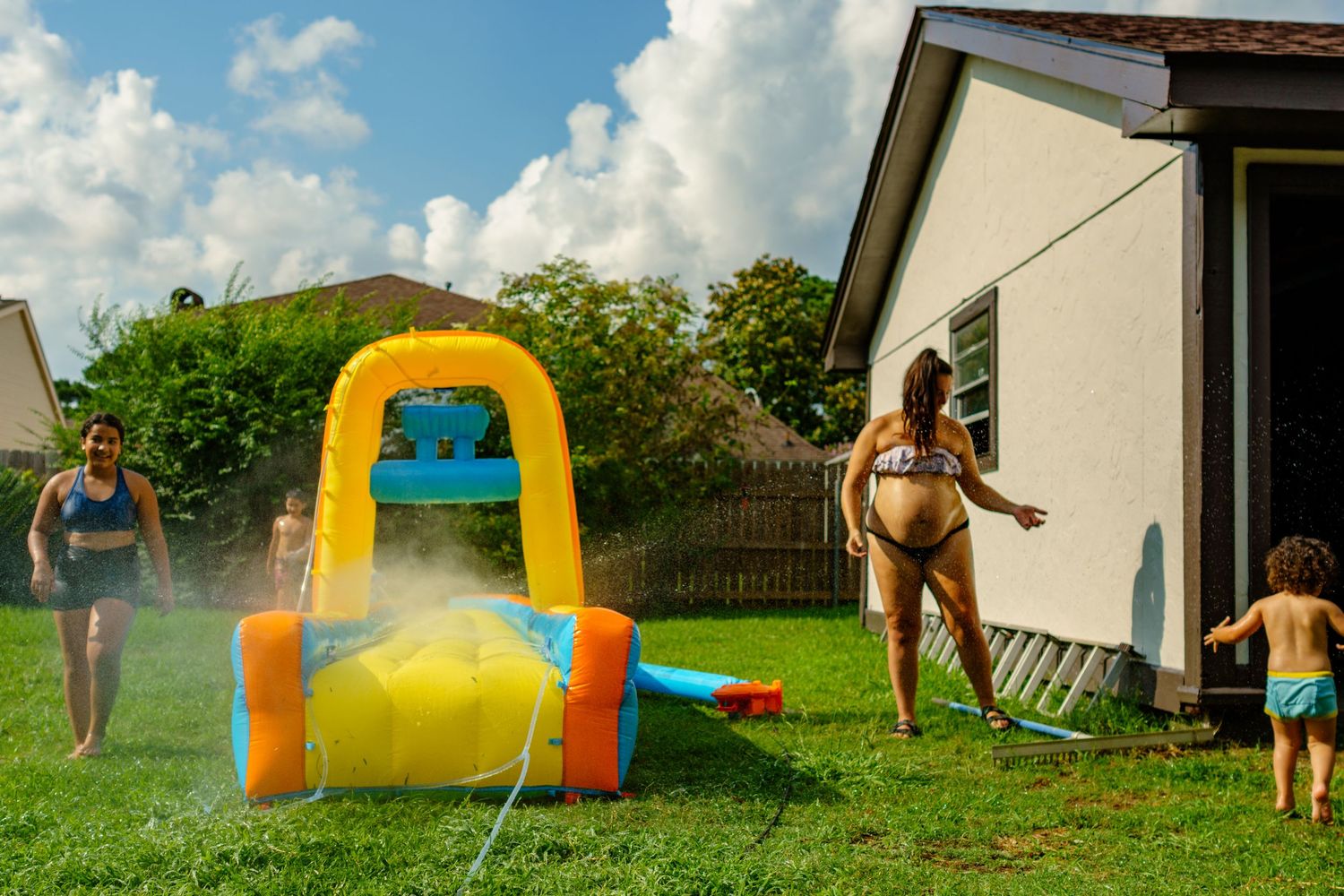 People enjoying summer fun in a backyard with an inflatable water slide and sprinklers on a sunny day.