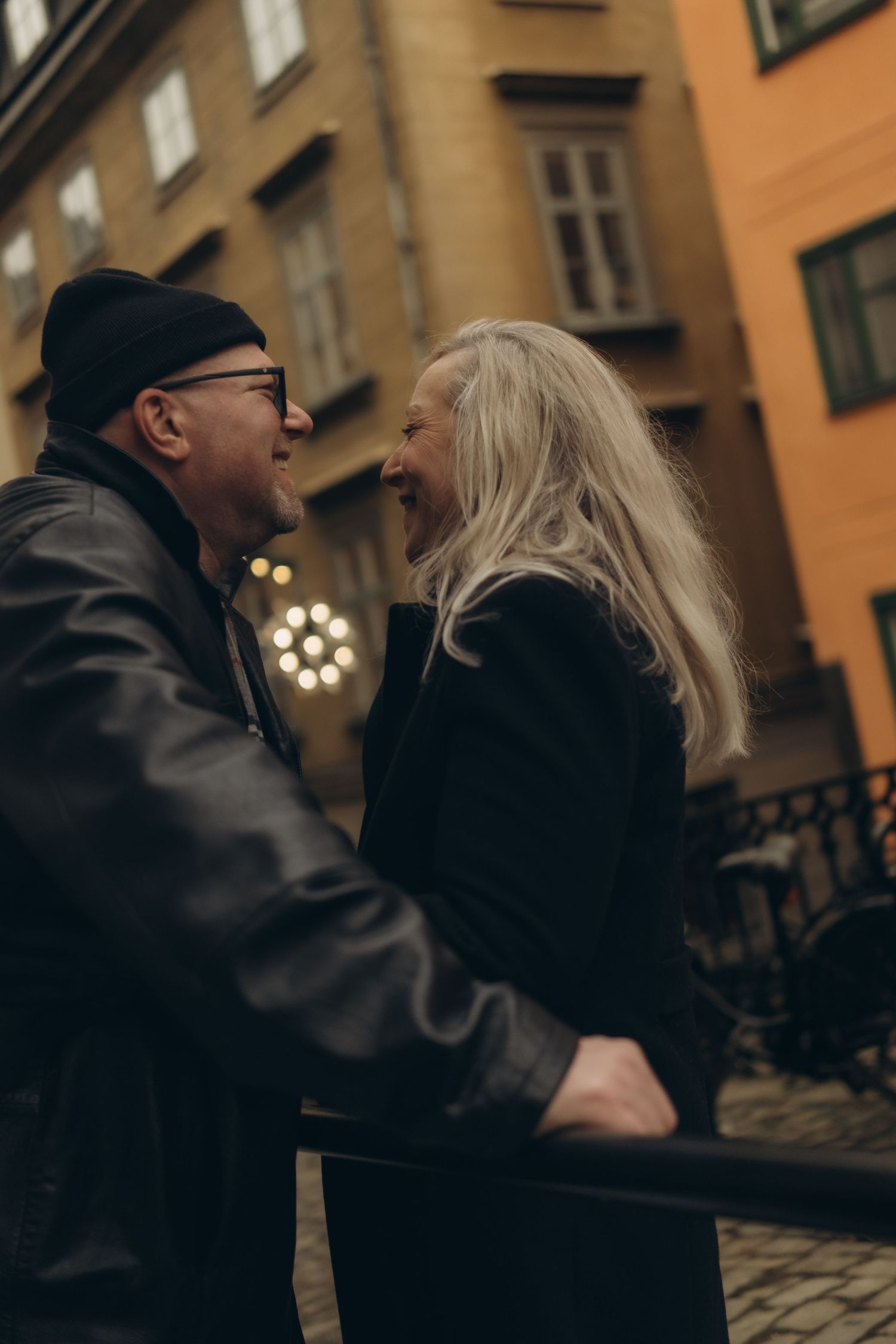 man and woman smiling at each other with Christmas light lit up behind them while being captured by vacation photographer in Stockholm