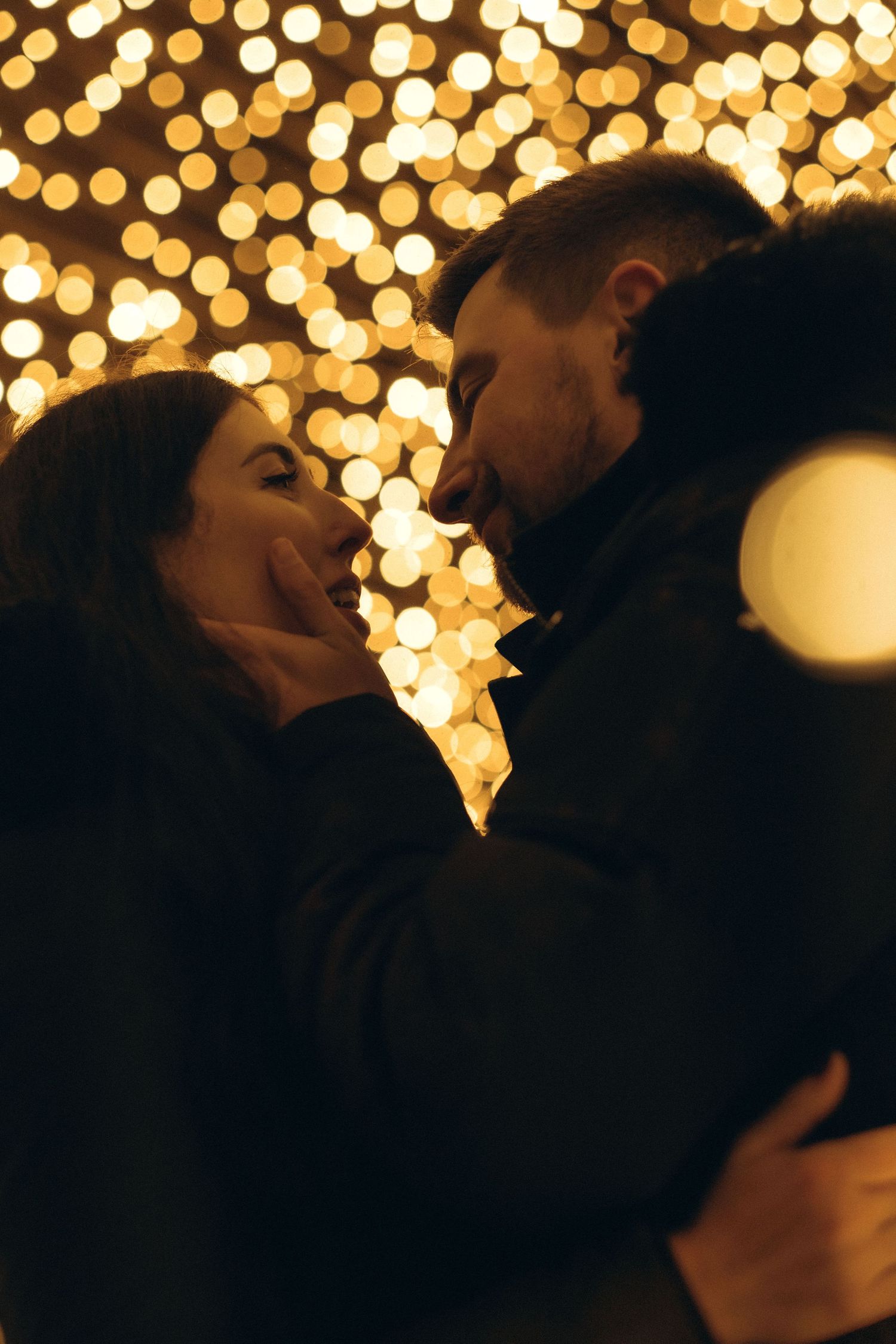 couple kissing with Christmas lights sparkling behind them during Christmas photoshoot in Stockholm