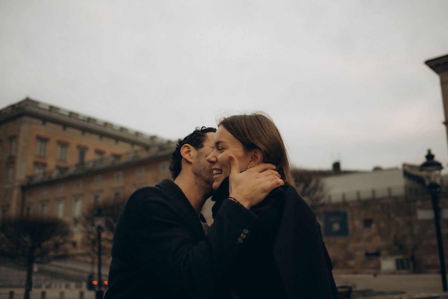 man grabbing his fiancée's face to kiss her while being captured by English-speaking engagement photographer in Stockholm