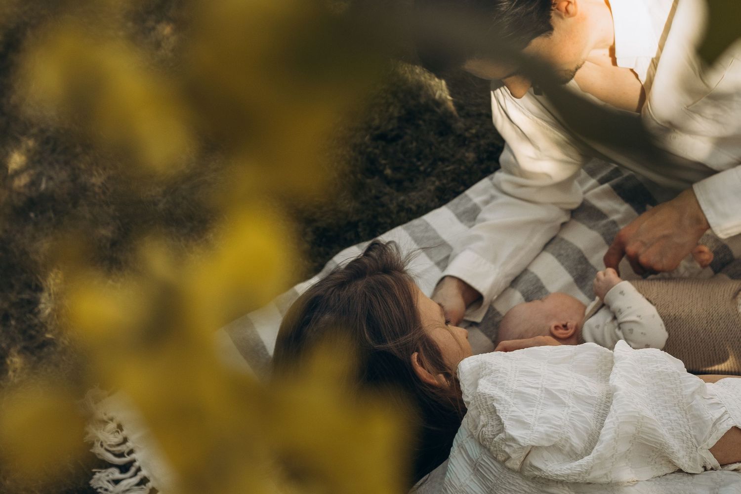 couple lying on blanket looking down at their newborn baby during garden family photoshoot in Stockholm