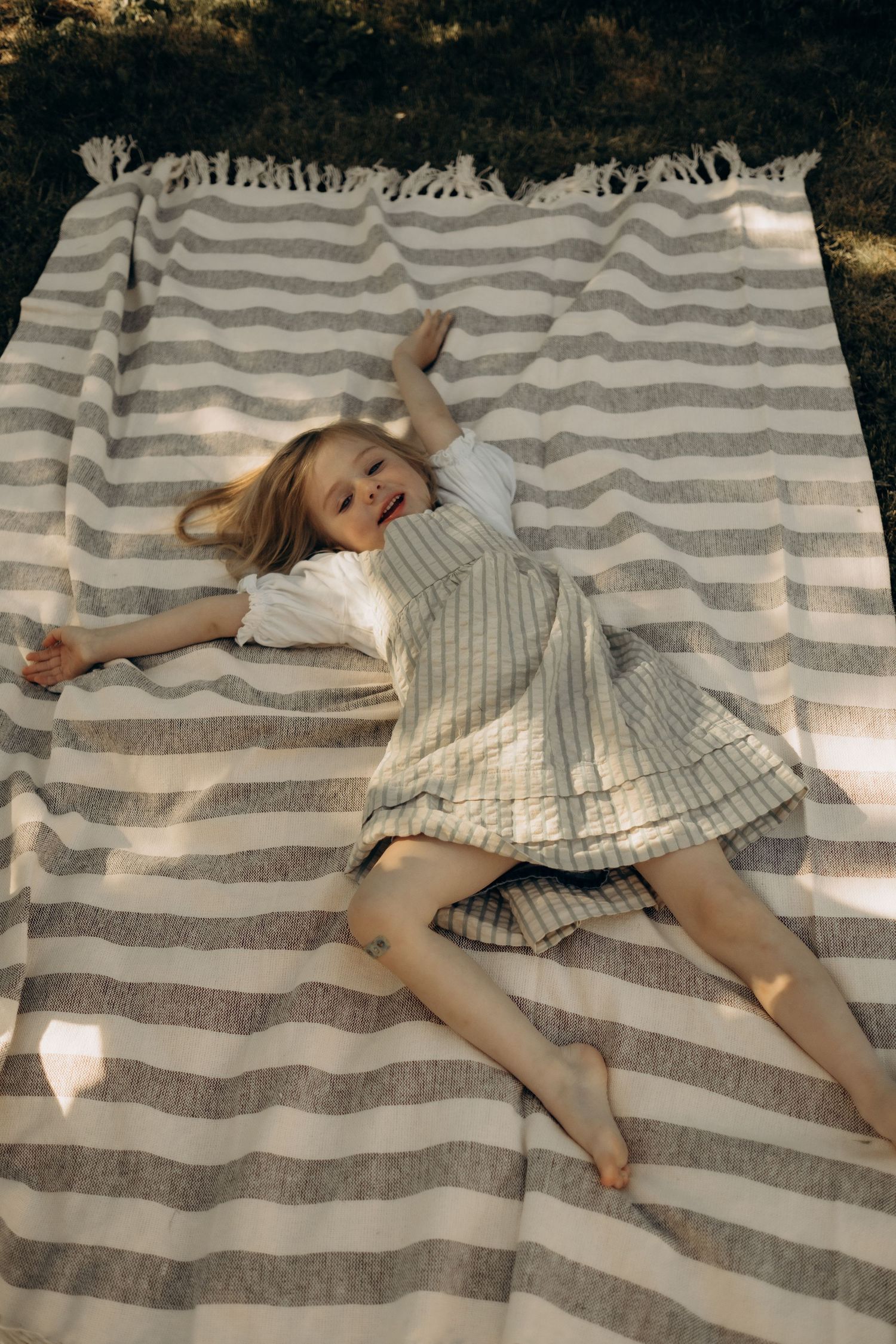 Little girl lying on picnic blanket during cozy garden family session in Stockholm. Relaxed, cinematic outdoor photoshoot.