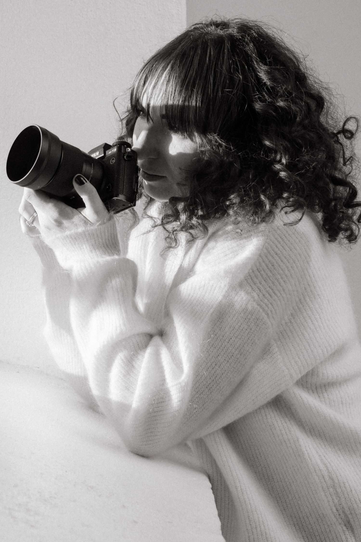 Stockholm photographer holding a camera to her face and looking out of the window while sun hits her face
