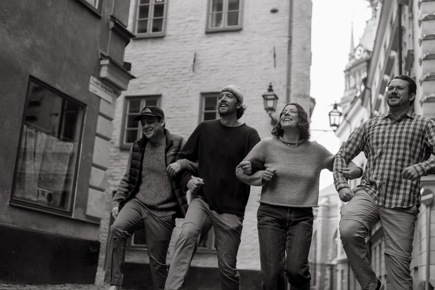 4 adult siblings holding hands and silly walking in Gamla Stan captured by photographer for family vacation in Stockholm