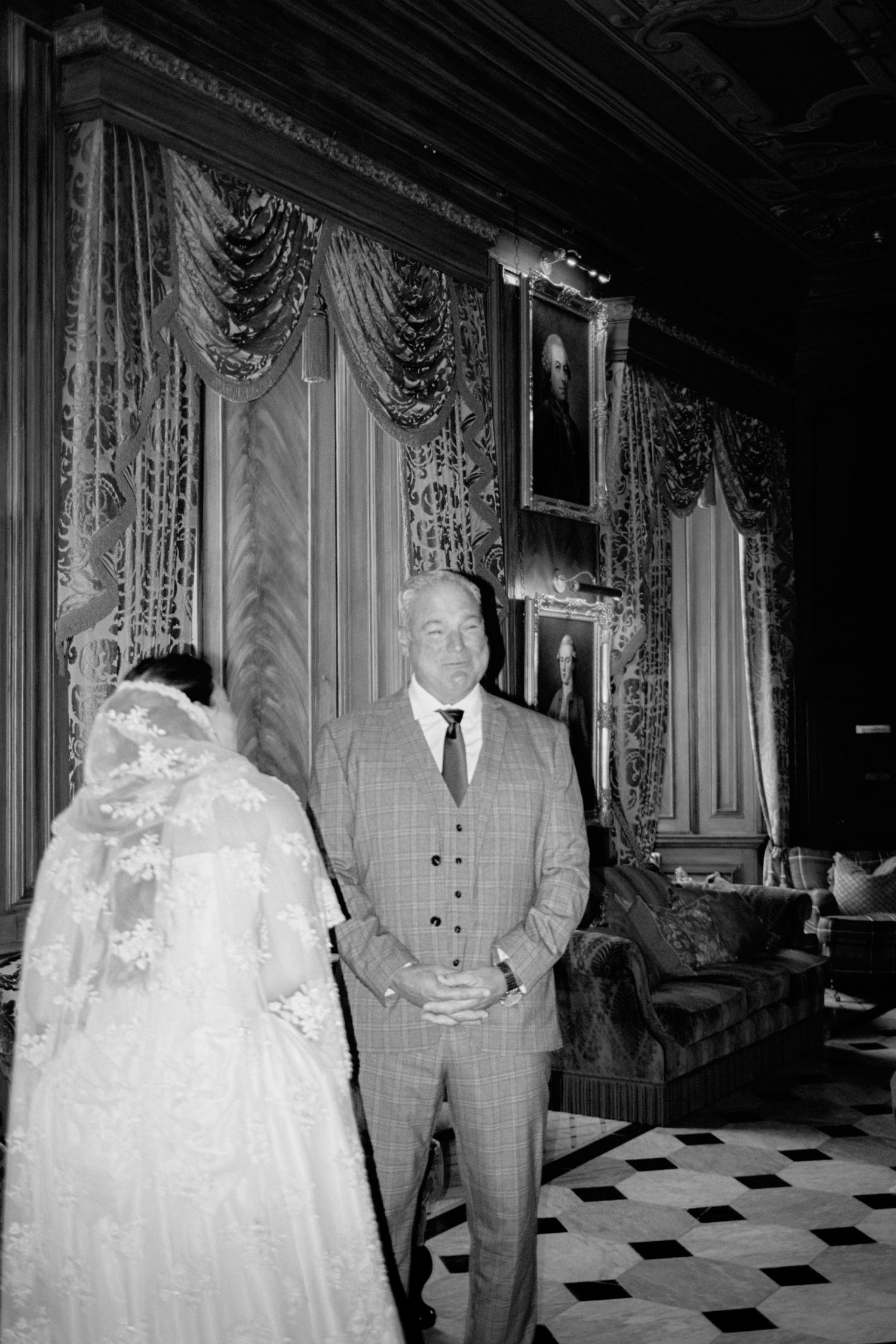 A formal black and white photograph showing people in wedding attire on a checkered floor.