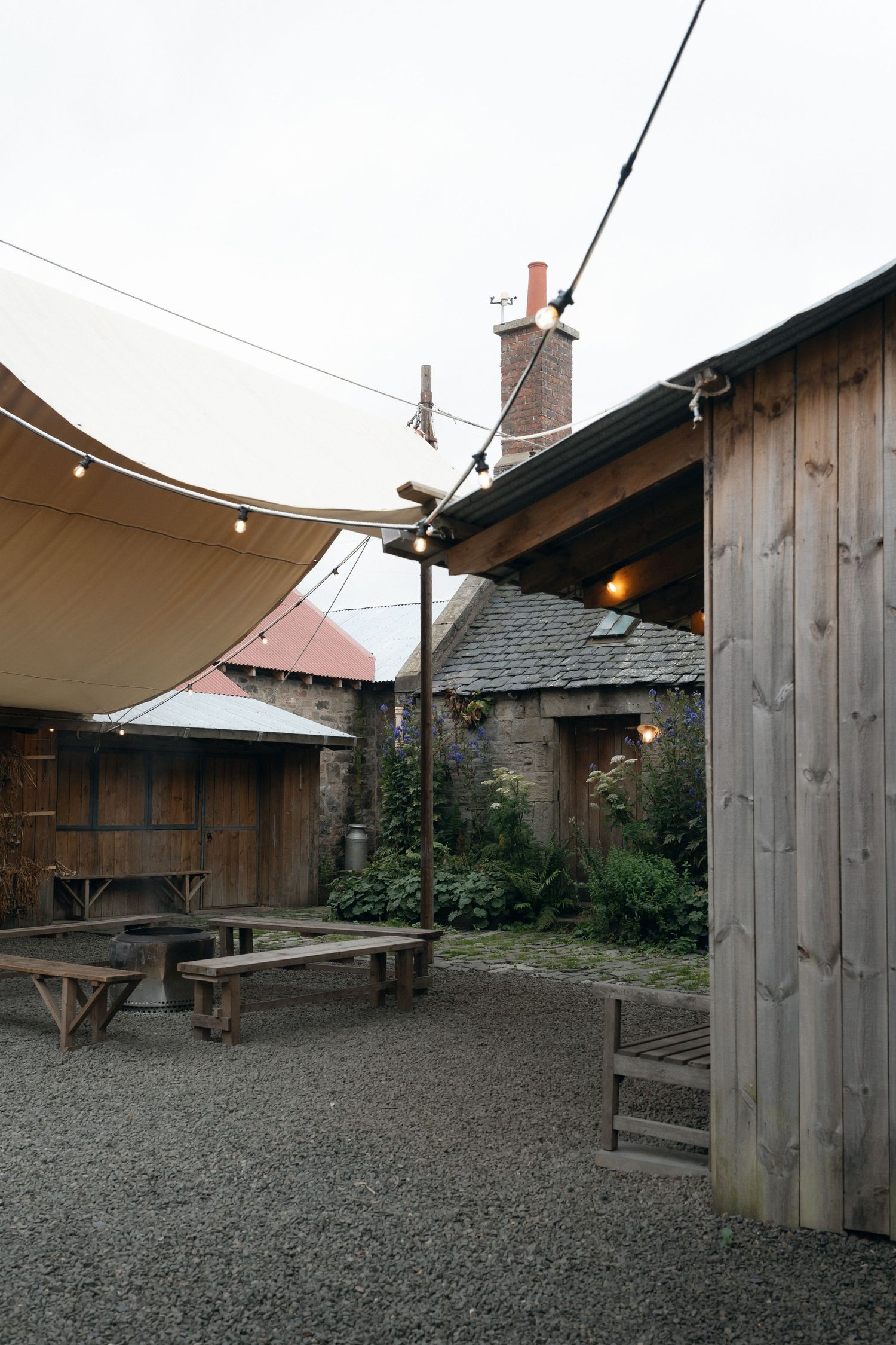 Rustic wooden buildings with gravel courtyard and covered walkways create an atmospheric outdoor space.