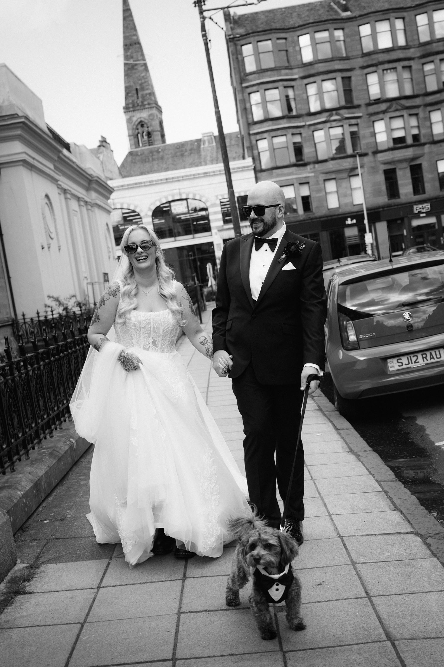 Bride and groom walking their dog on a city sidewalk in black and white wedding photo.