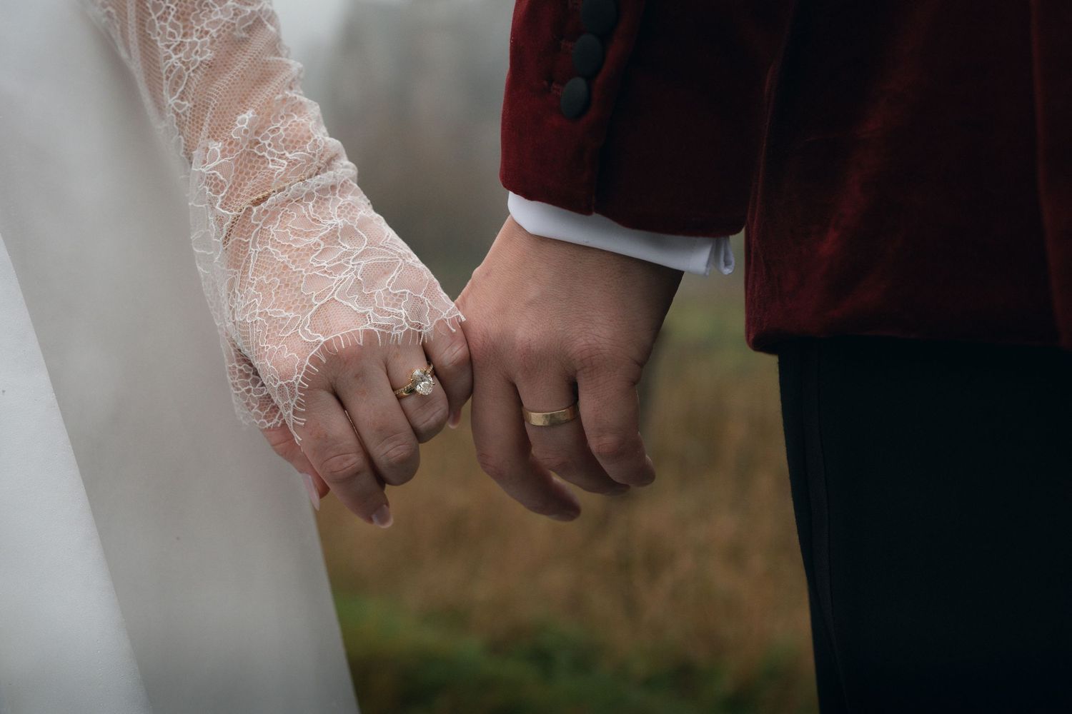 Two hands wearing white lace gloves gently touch in a romantic outdoor setting with a blurred background.