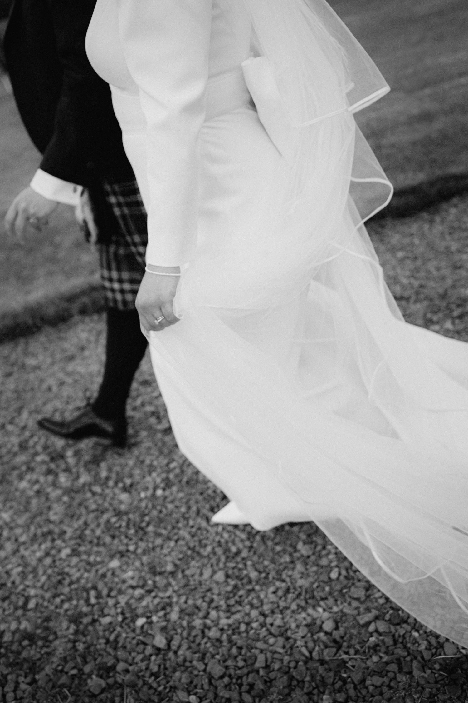 A black and white photo captures flowing wedding dress fabric and traditional Scottish kilt in motion.