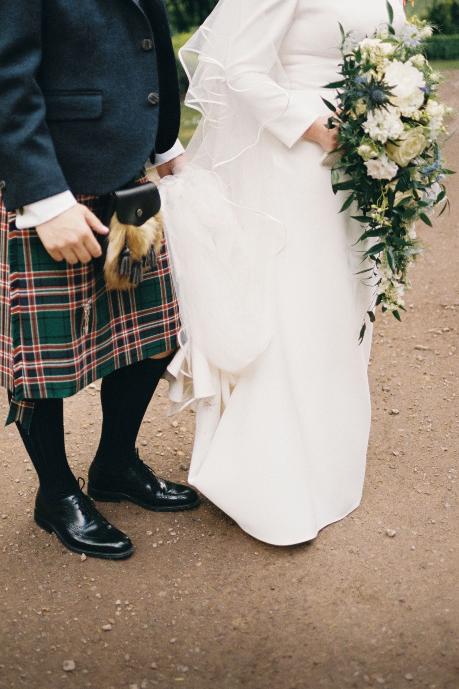 Wedding party members in traditional Scottish kilts and dress shoes stand next to a flowing white wedding gown.