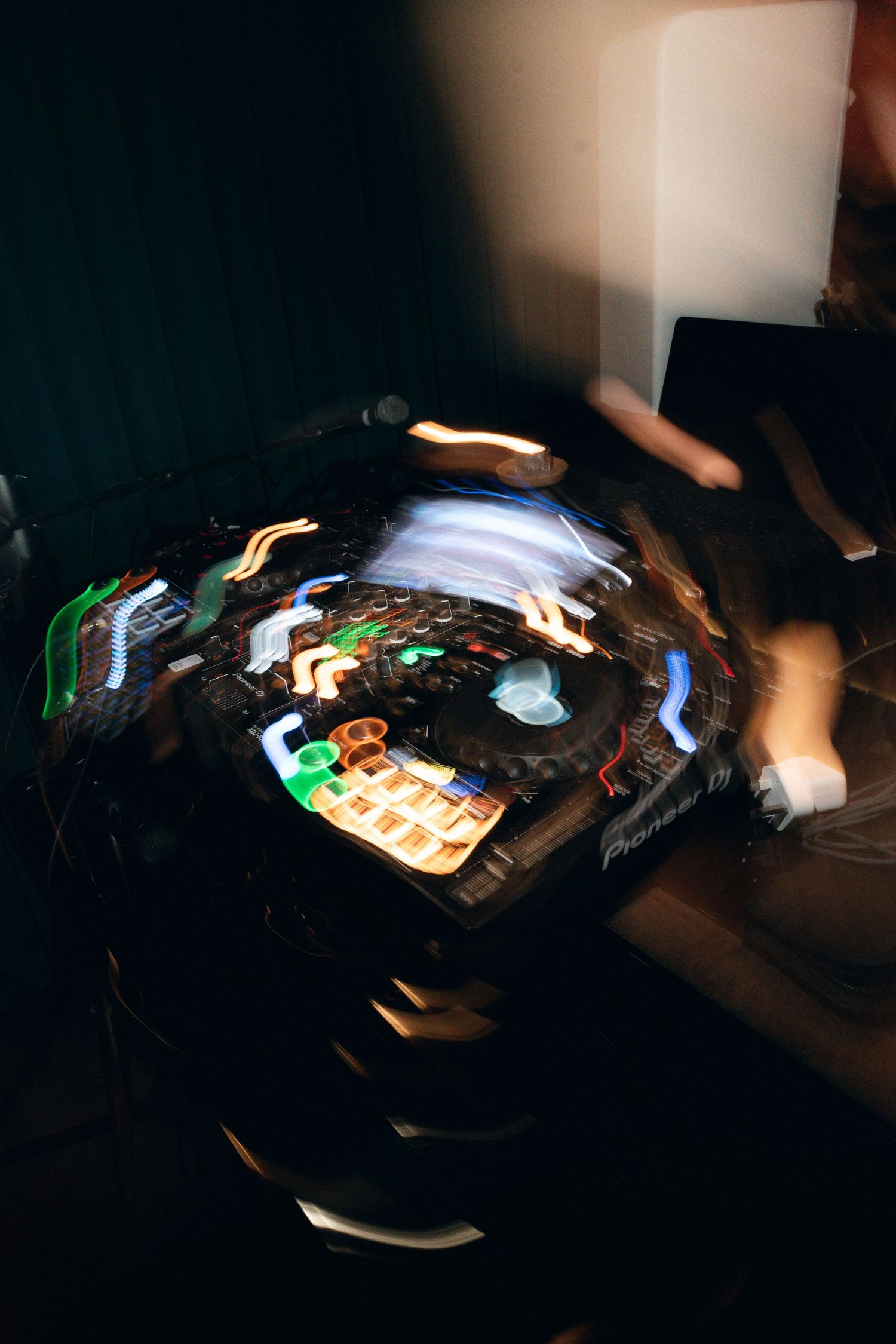 DJ mixing on a Pioneer controller with colorful light trails in a dark nightclub setting.