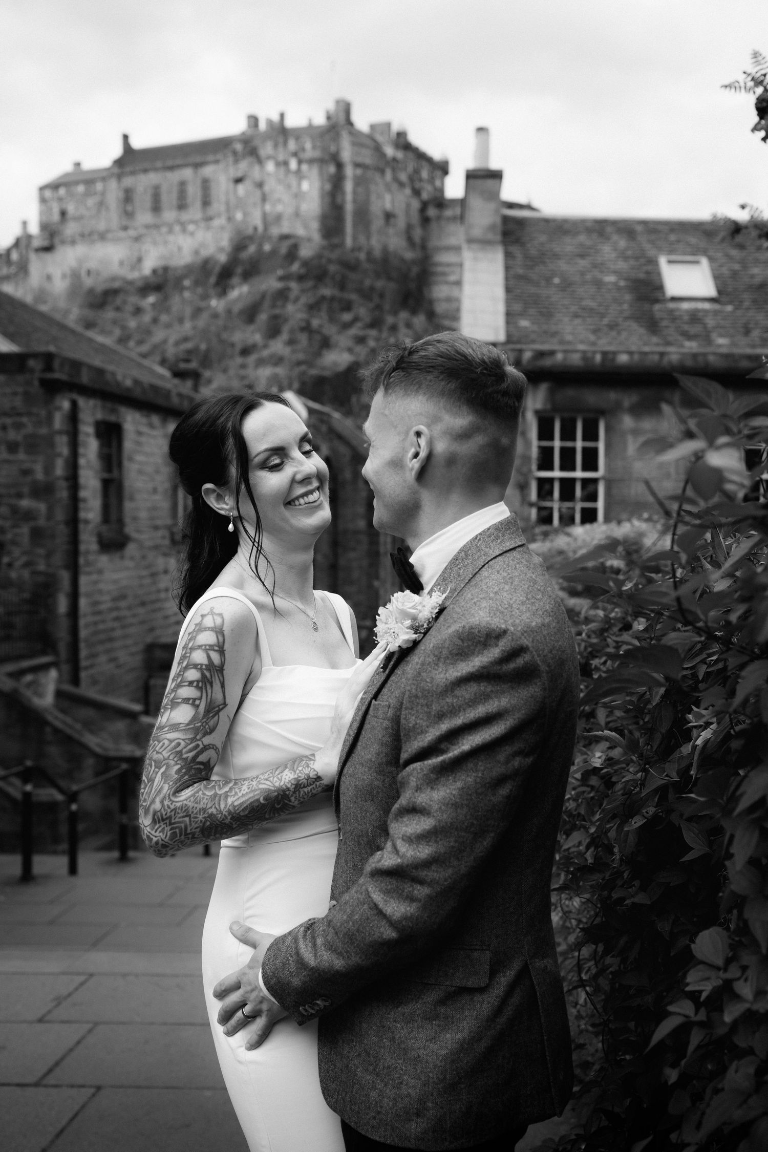 A romantic wedding moment captured in black and white with Edinburgh Castle looming dramatically in the background.
