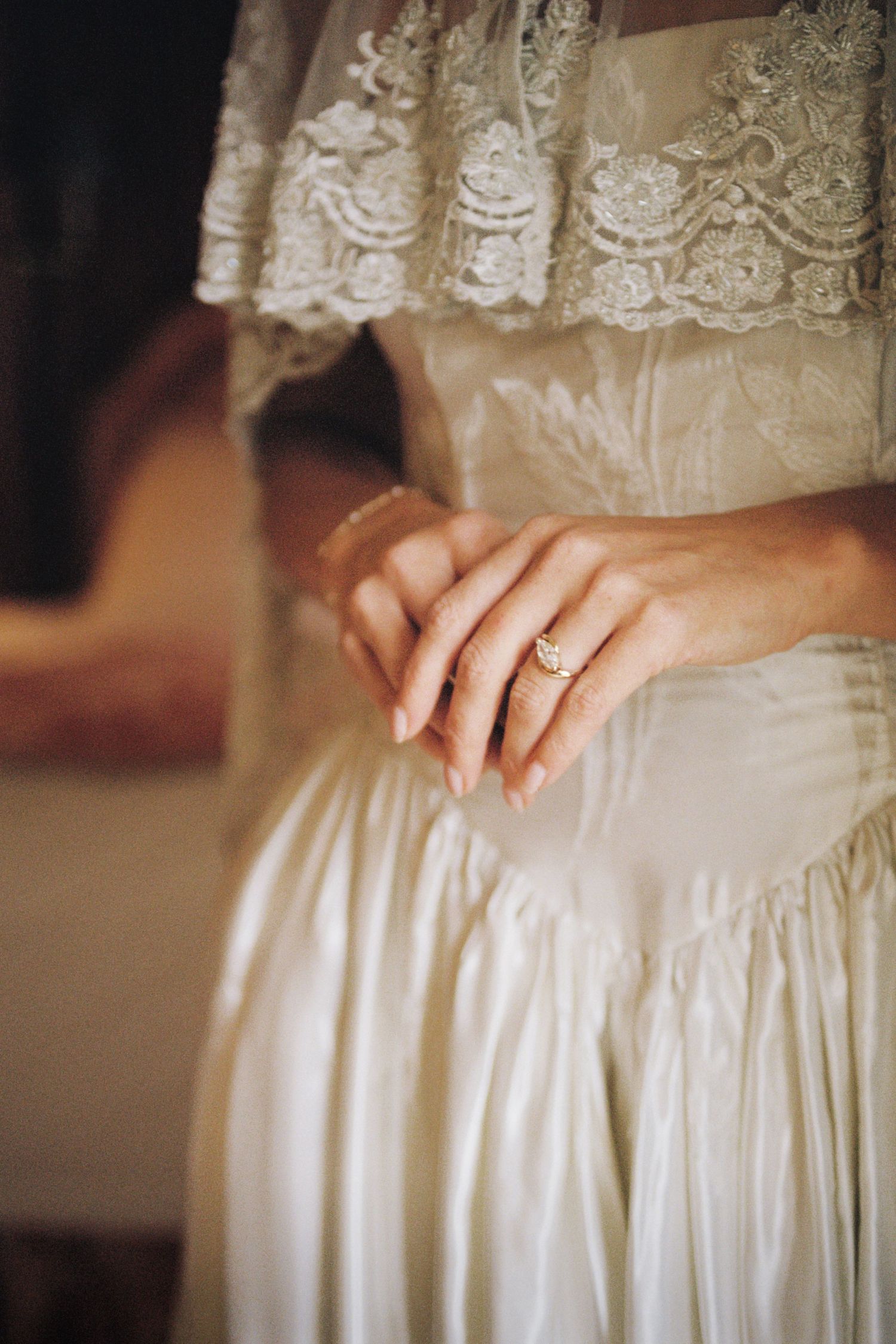 Close-up detail of hands resting on a white lace wedding dress with gathered fabric texture.