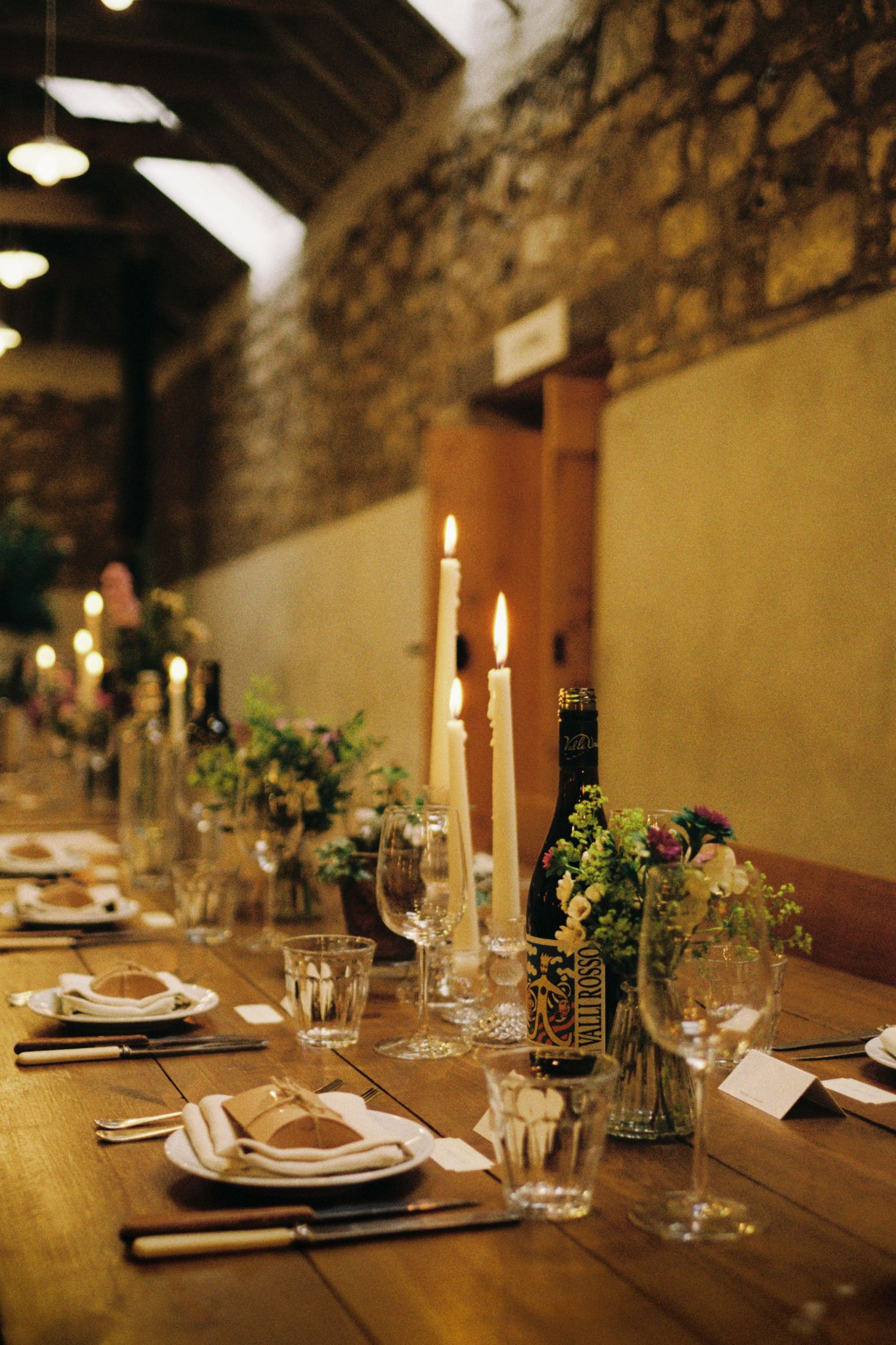 Elegant table setting with white candles and greenery in a rustic stone-walled restaurant interior.