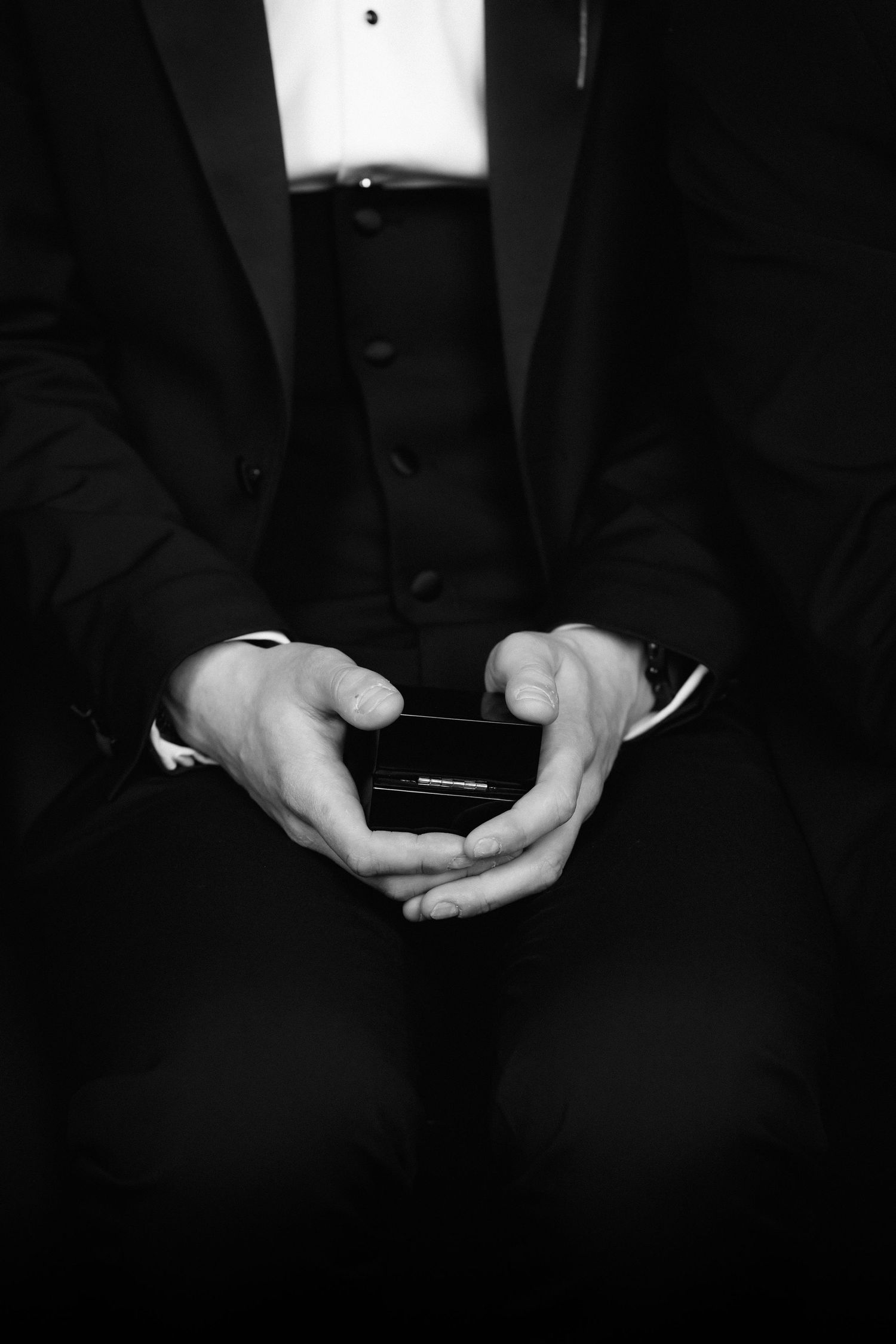 Man in tuxedo holding a small jewelry box in cupped hands, black and white photo.