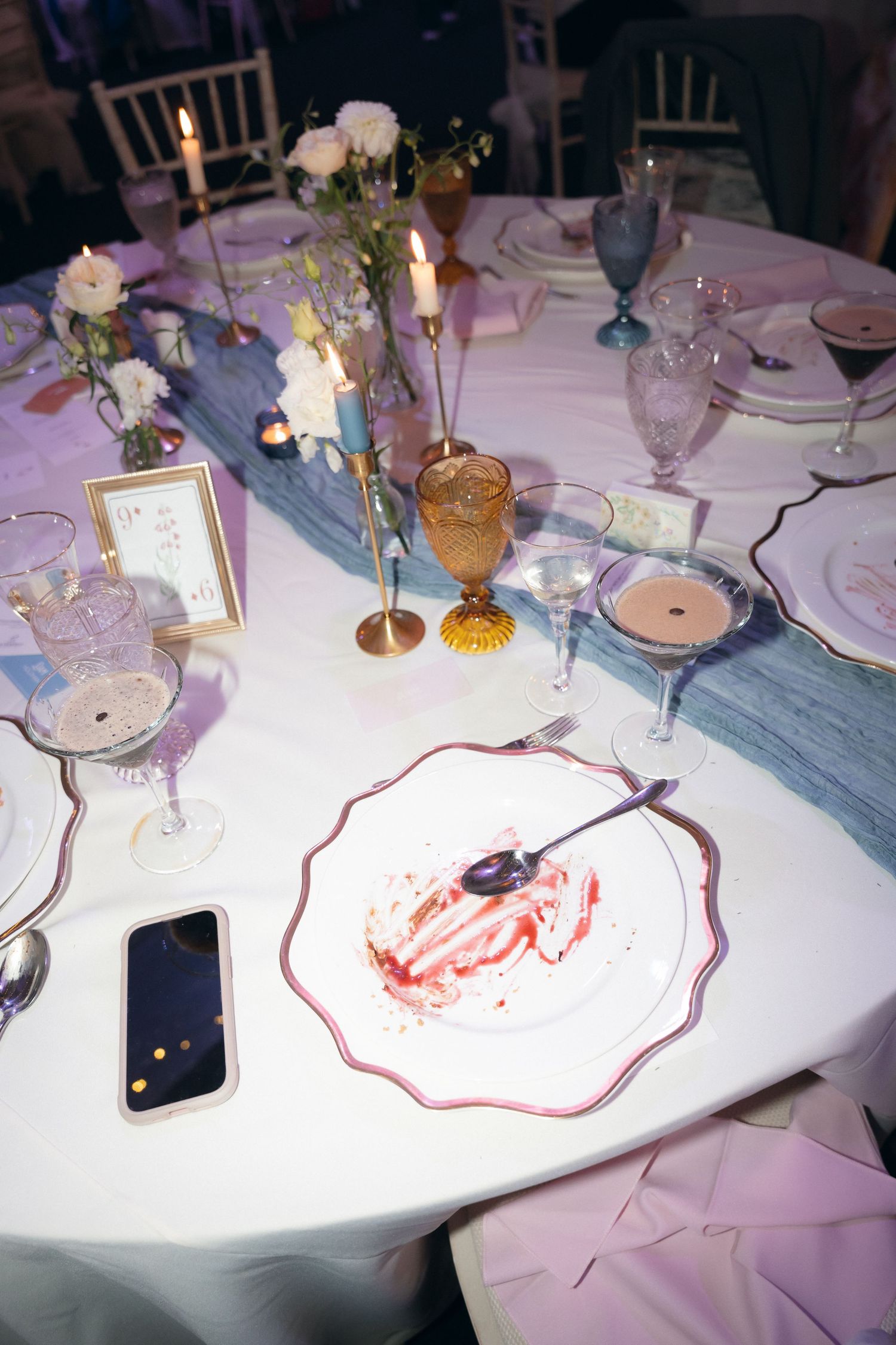 Elegant table settings at a formal dinner with white linens, candles, and red decorative patterns.