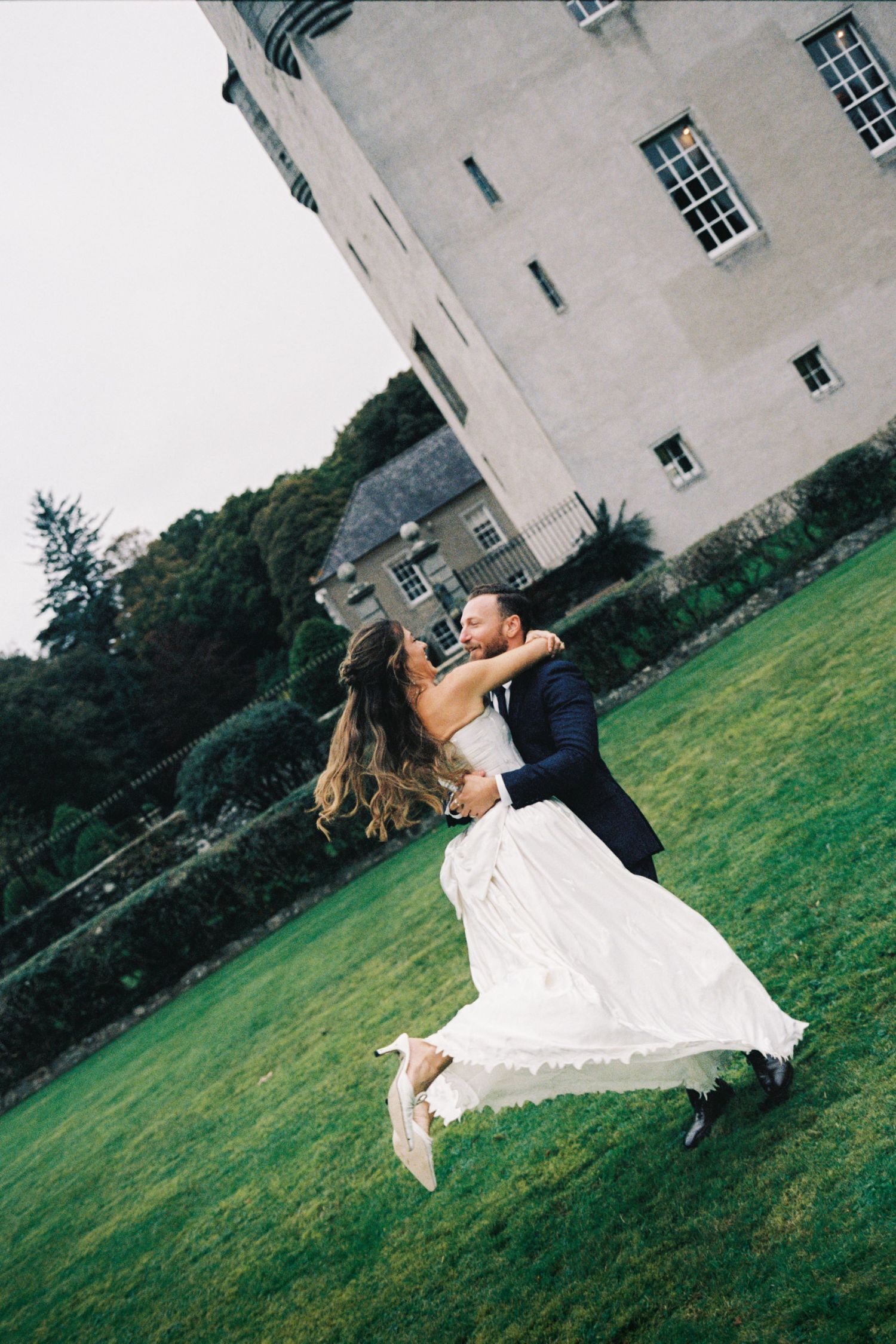 A couple dancing and twirling on a green lawn outside a grand white building.