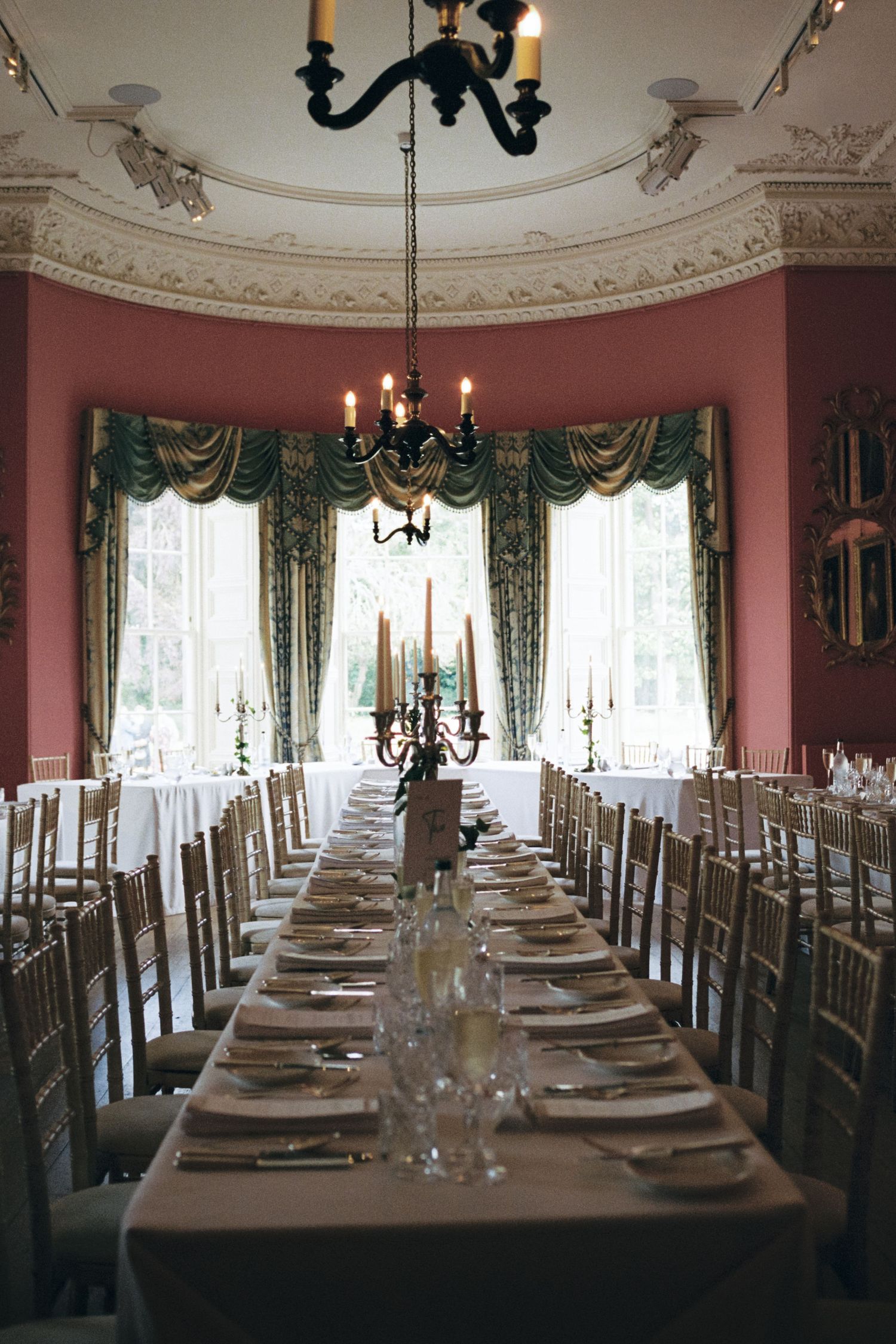 Elegant dining room panorama with long table set for formal dinner featuring crystal candelabras and green drapery.
