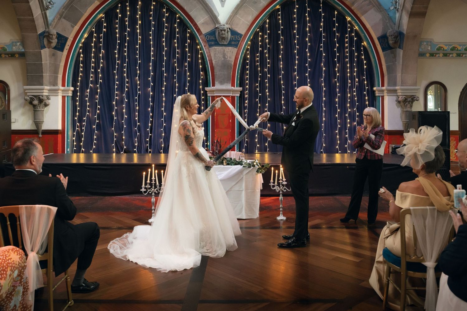 Bride and groom exchange vows in an elegant church ceremony with fairy lights and guests seated nearby.