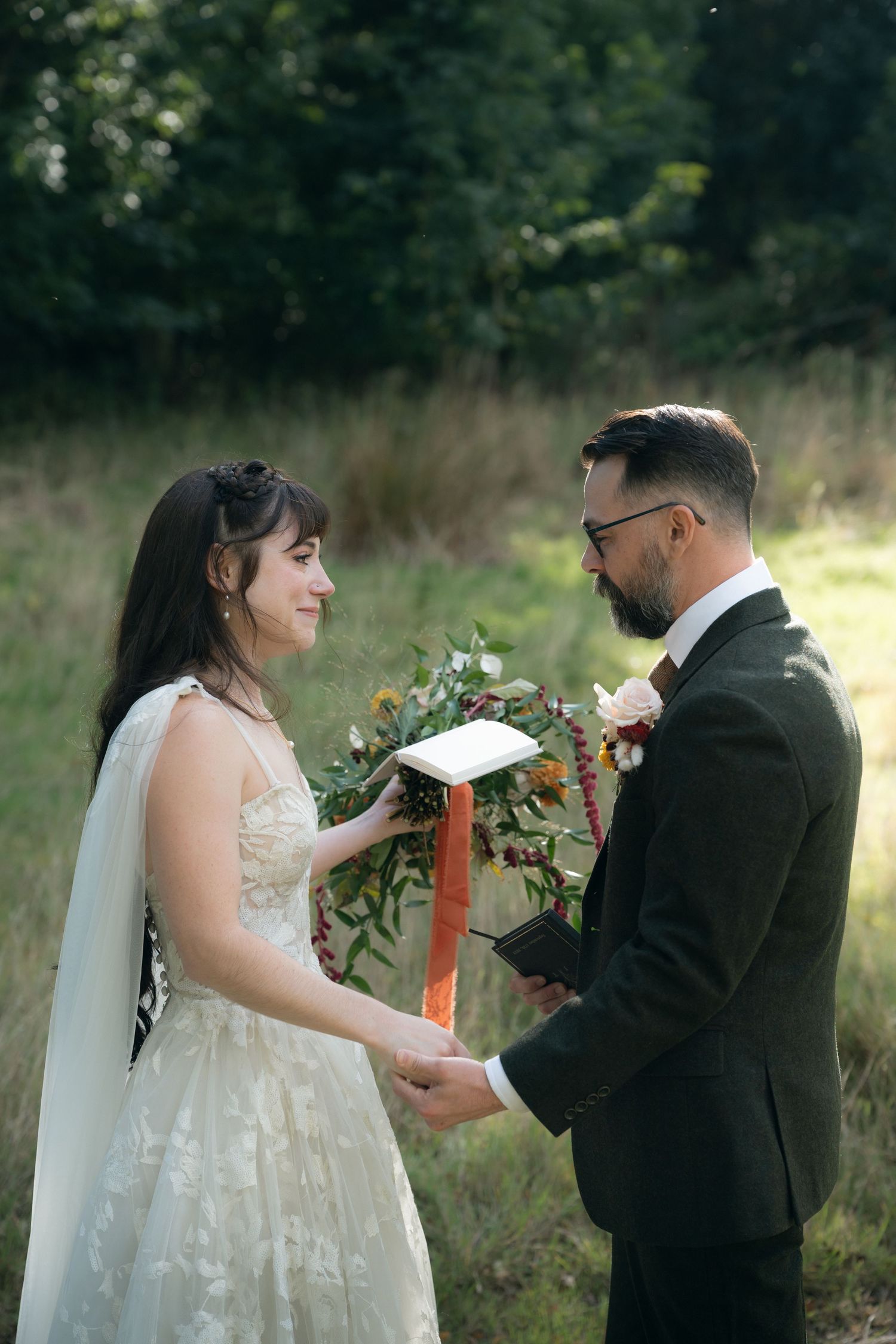 A bride and groom share a candid moment during their outdoor wedding photo session in a sunlit field.
