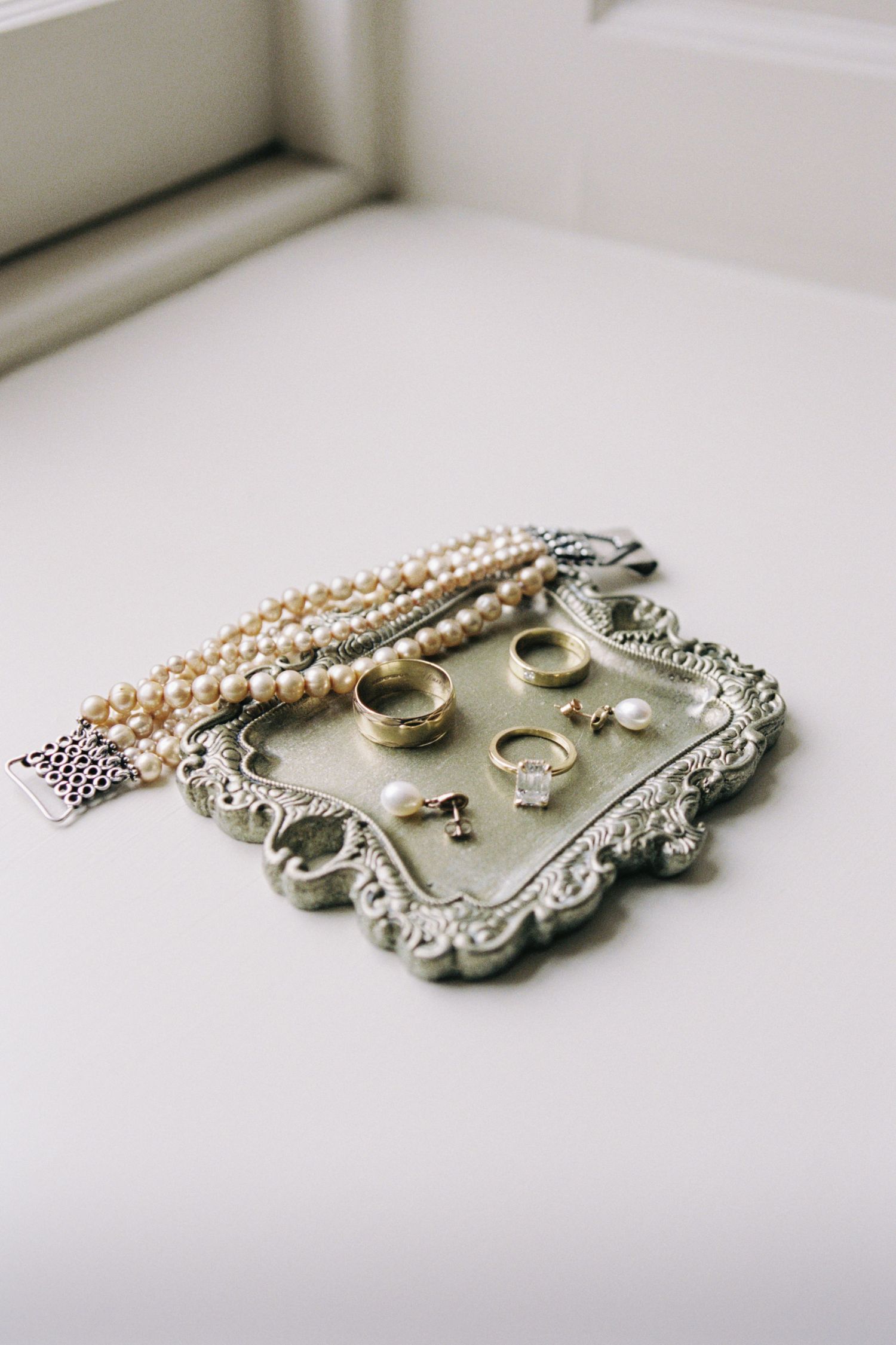 Elegant vintage-style silver jewelry tray with pearls and accessories arranged in a minimalist composition on white surface.