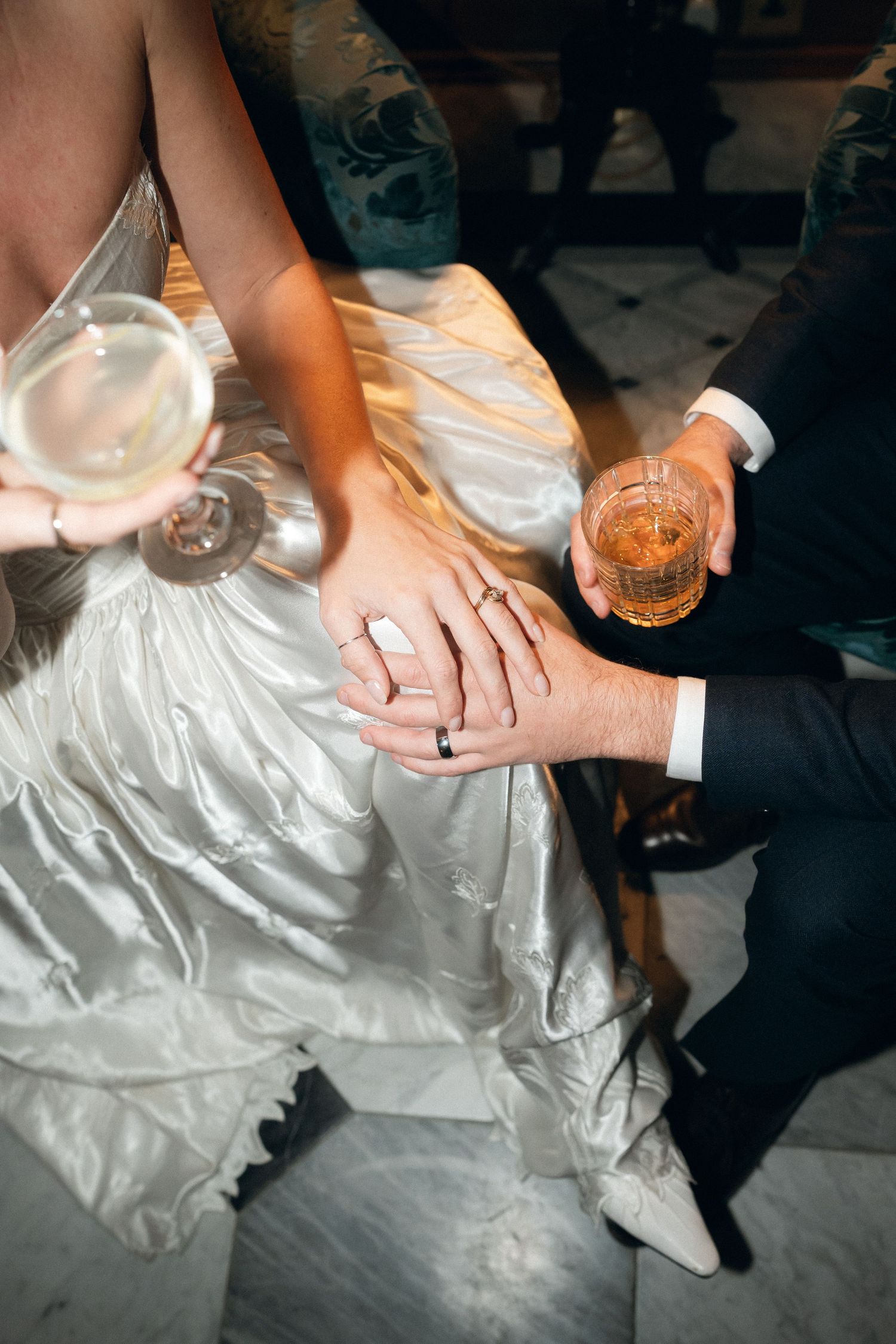 Close-up shots of hands holding drinks while wearing formal wedding attire at a reception celebration.