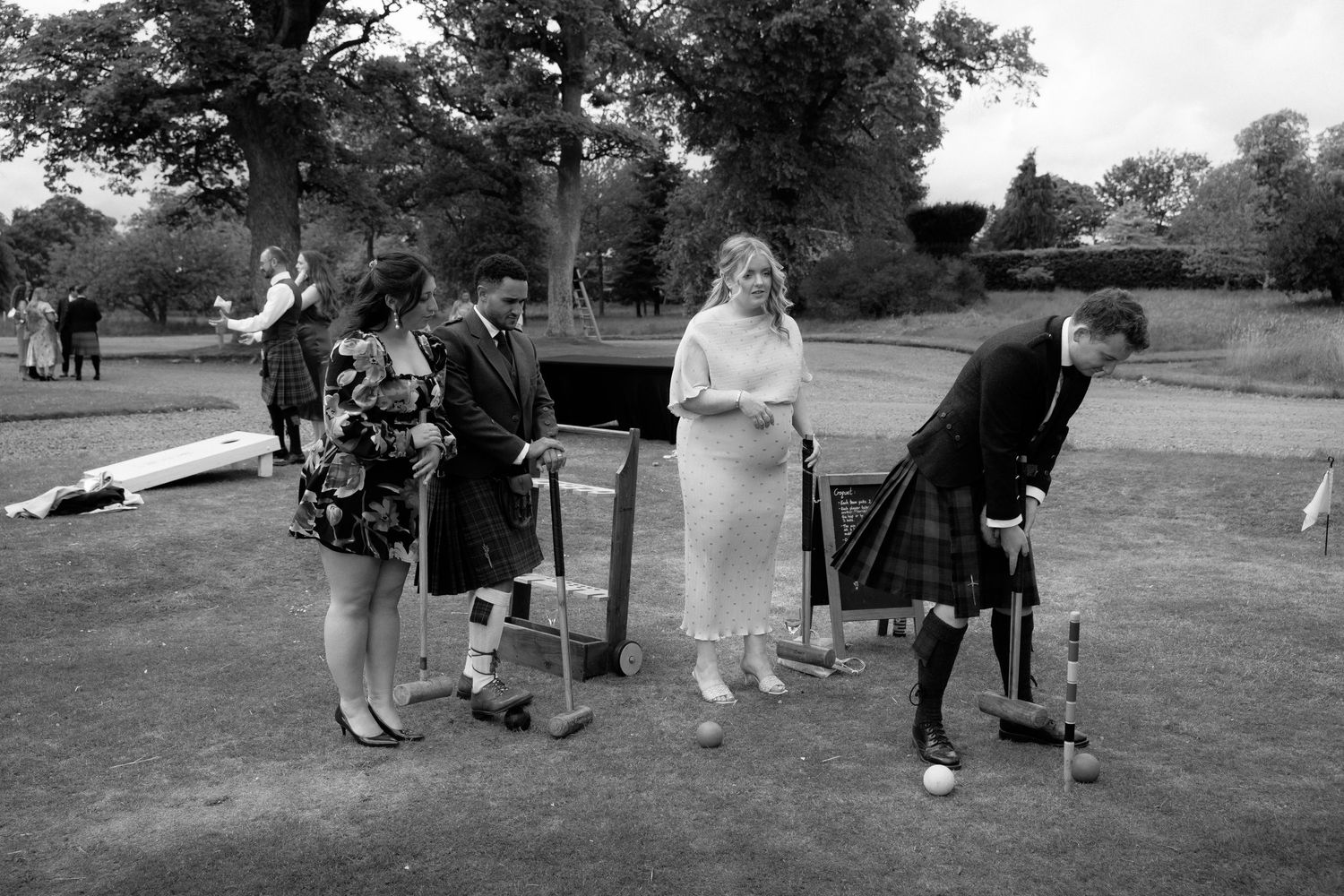 A group of people playing croquet on a lawn during an outdoor social gathering.