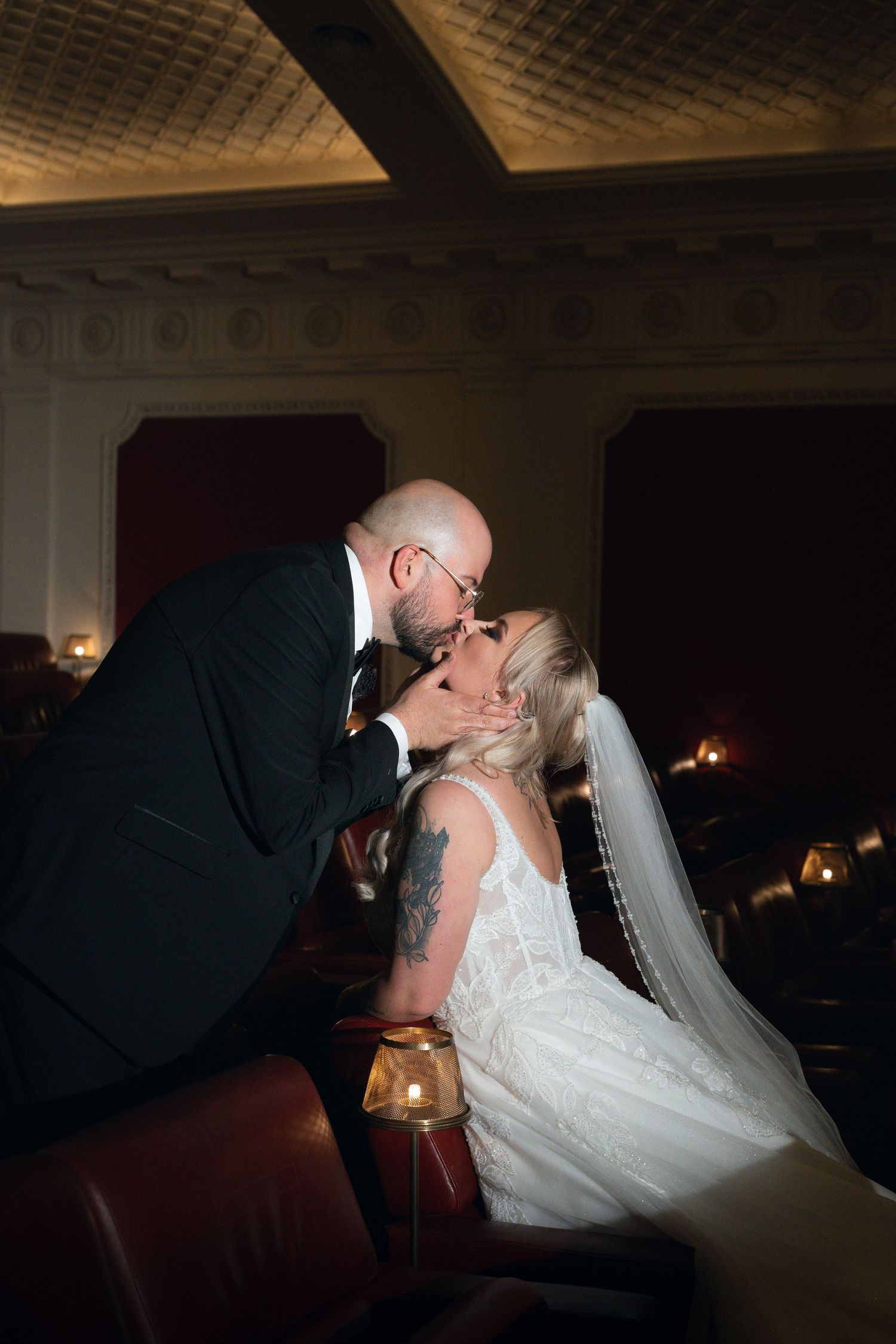 A bride and groom share a romantic first kiss during their wedding ceremony in an elegantly lit venue.