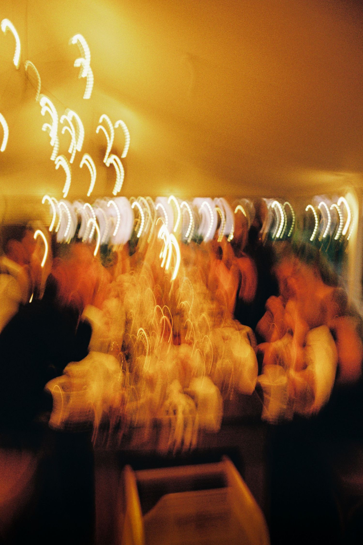 Long exposure photograph shows blurred motion of dancers at a party with warm golden lighting creating ethereal streaks.