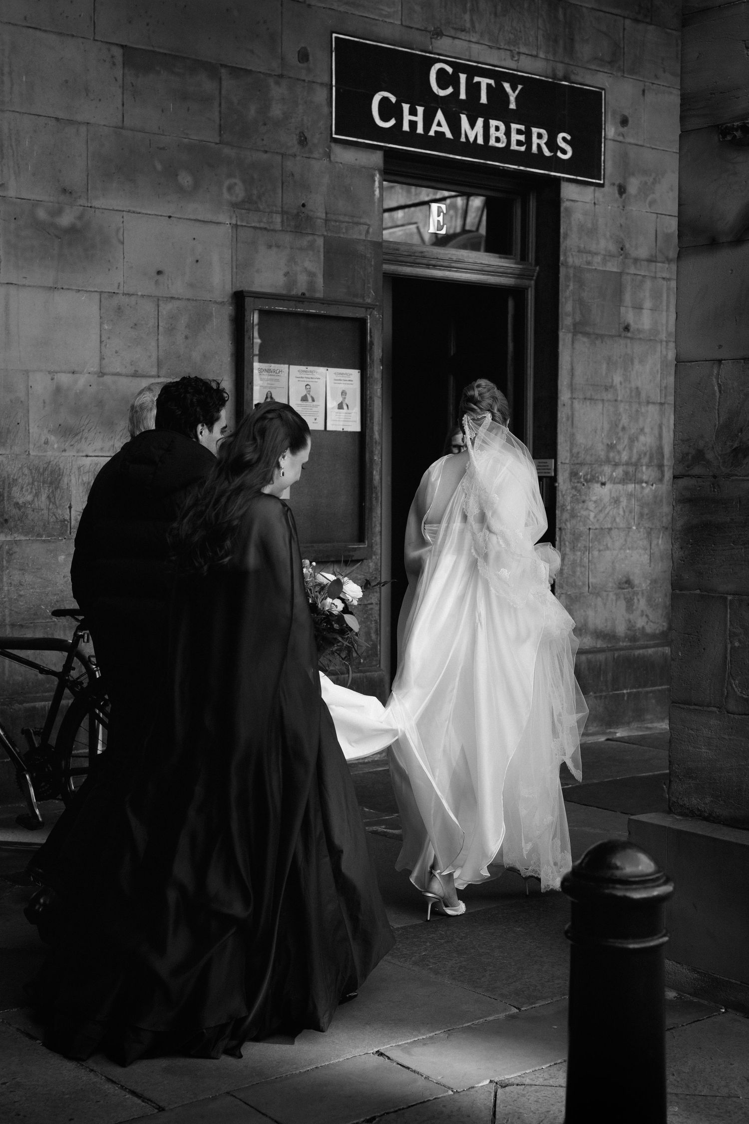 A sequence of black and white photos showing figures in dark coats entering a city chambers building.