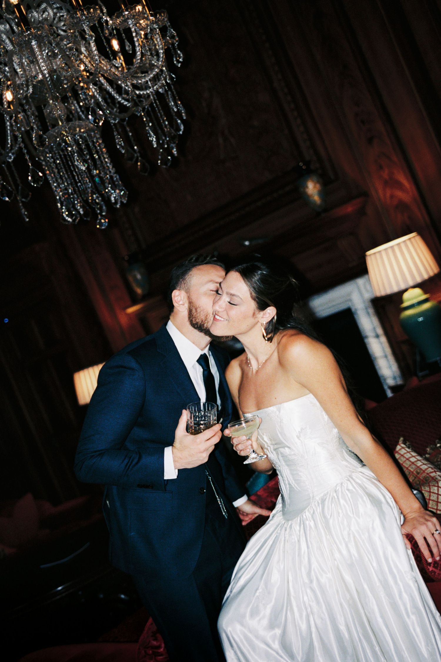 A romantic wedding couple shares an intimate kiss under an elegant crystal chandelier.