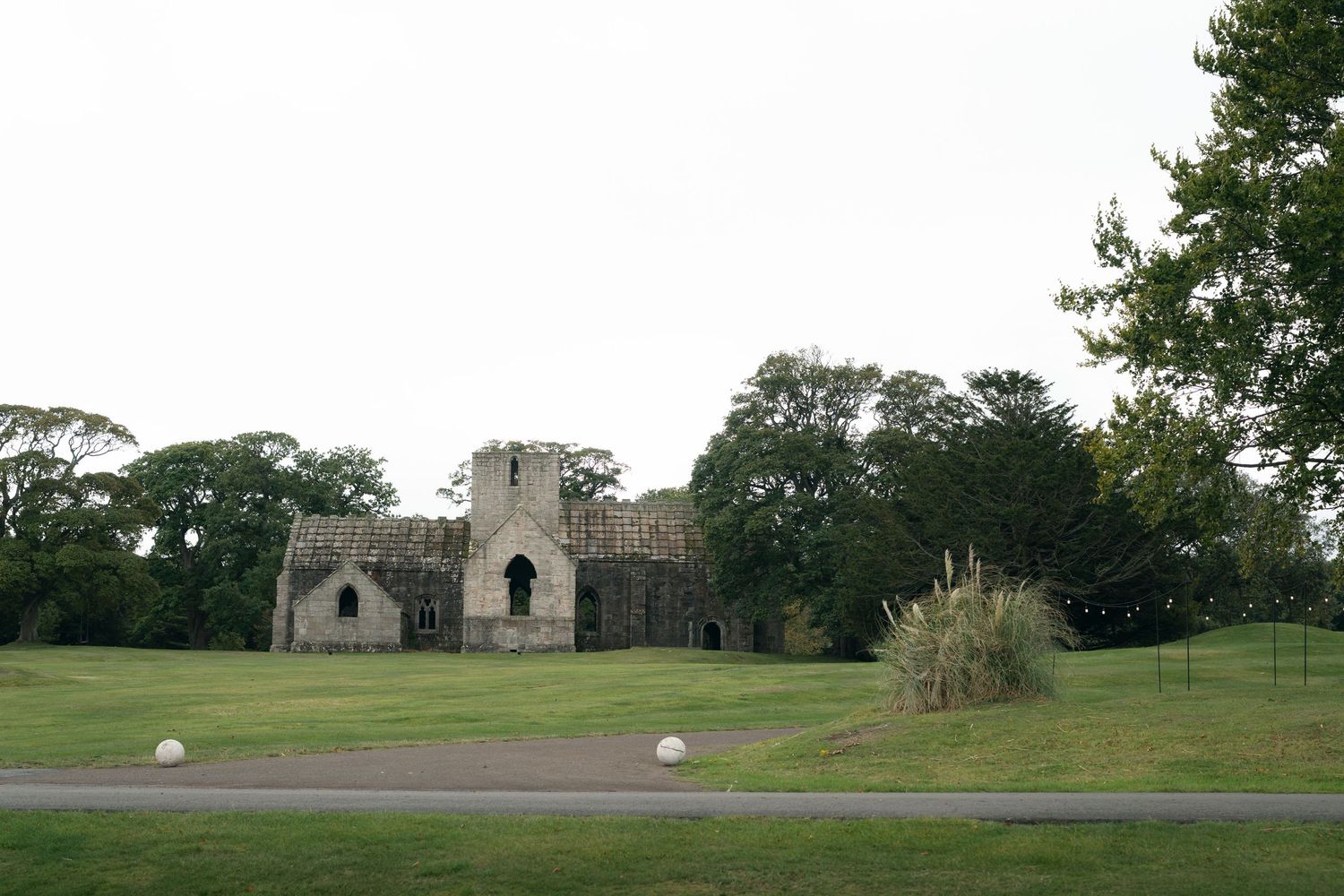 Ancient stone ruins of a castle or church stand against a green landscape under cloudy skies.