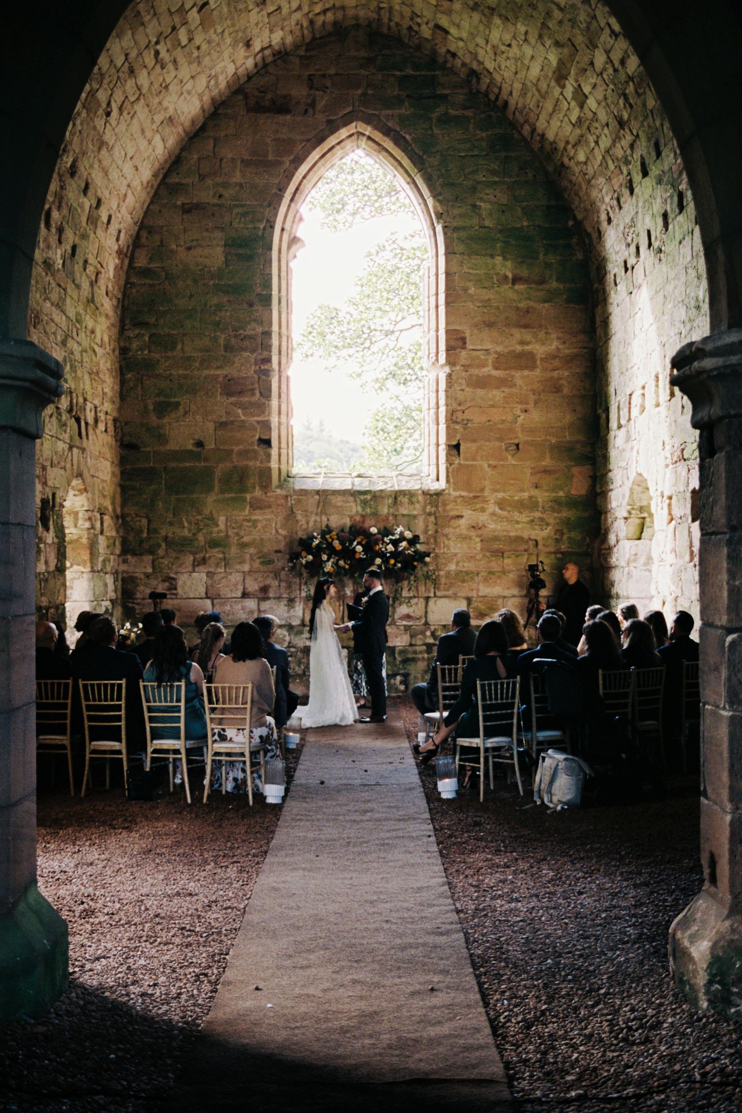 Stone archways frame a rustic indoor venue with chairs arranged for a wedding ceremony in a historic building.