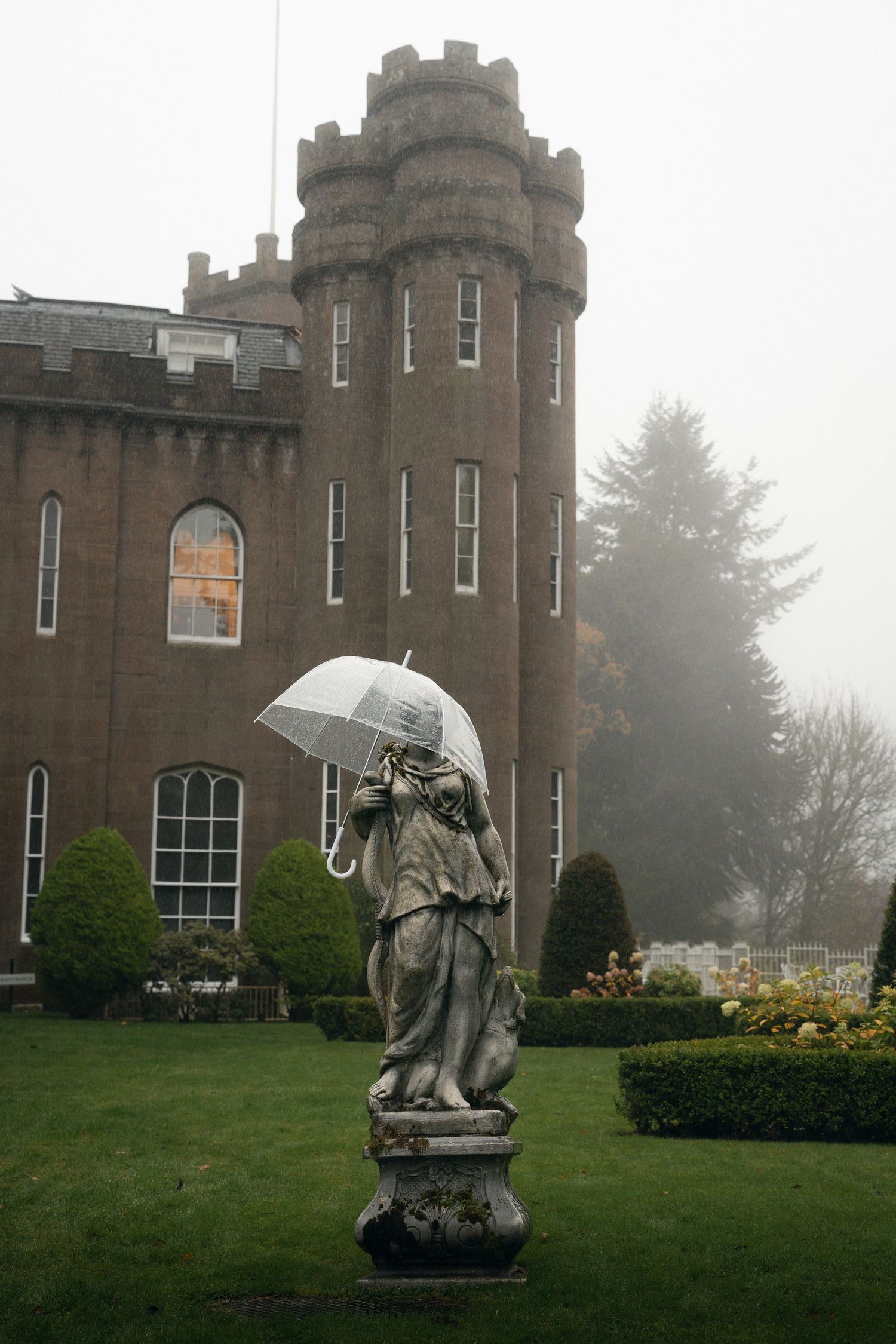 Stone statues stand guard on the misty grounds of a grand castle with turrets and towers.