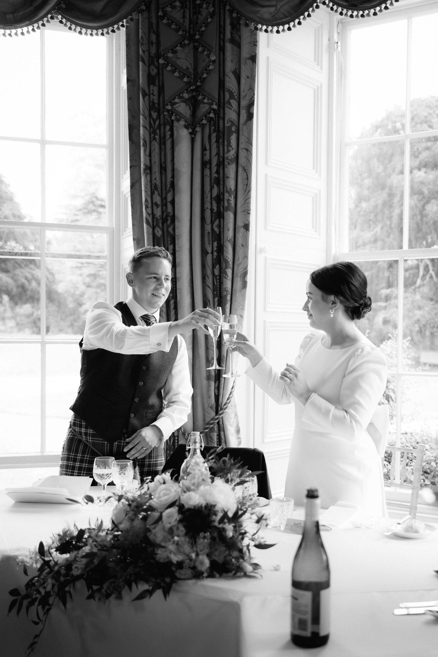 A celebratory toast between two people at an elegant table with floral centerpiece.