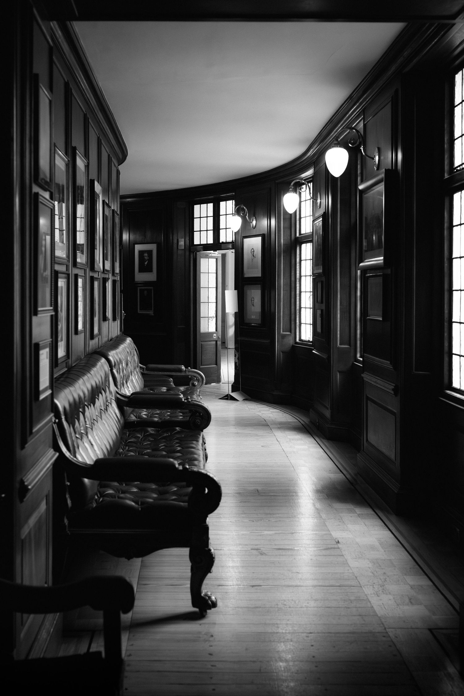 A dark moody hallway with vintage furniture and large windows creating dramatic shadows and light patterns.